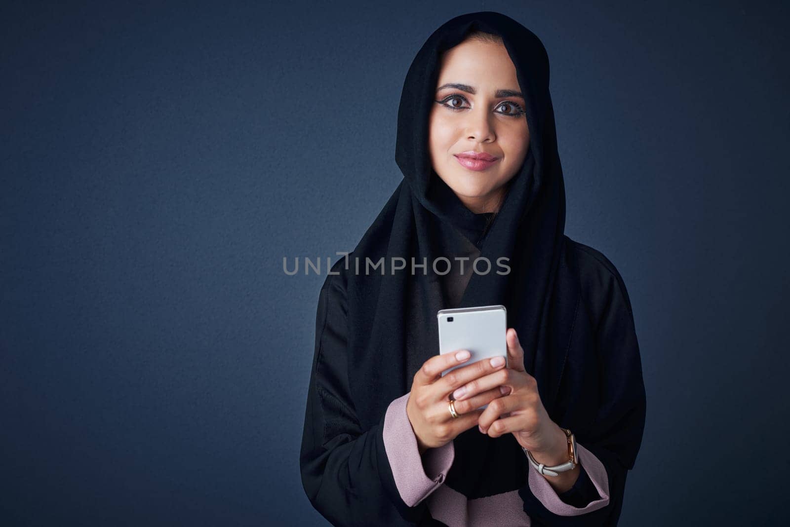 Im connected, lets chat. Studio portrait of a young woman wearing a burqa and using a mobile phone against a gray background. by YuriArcurs