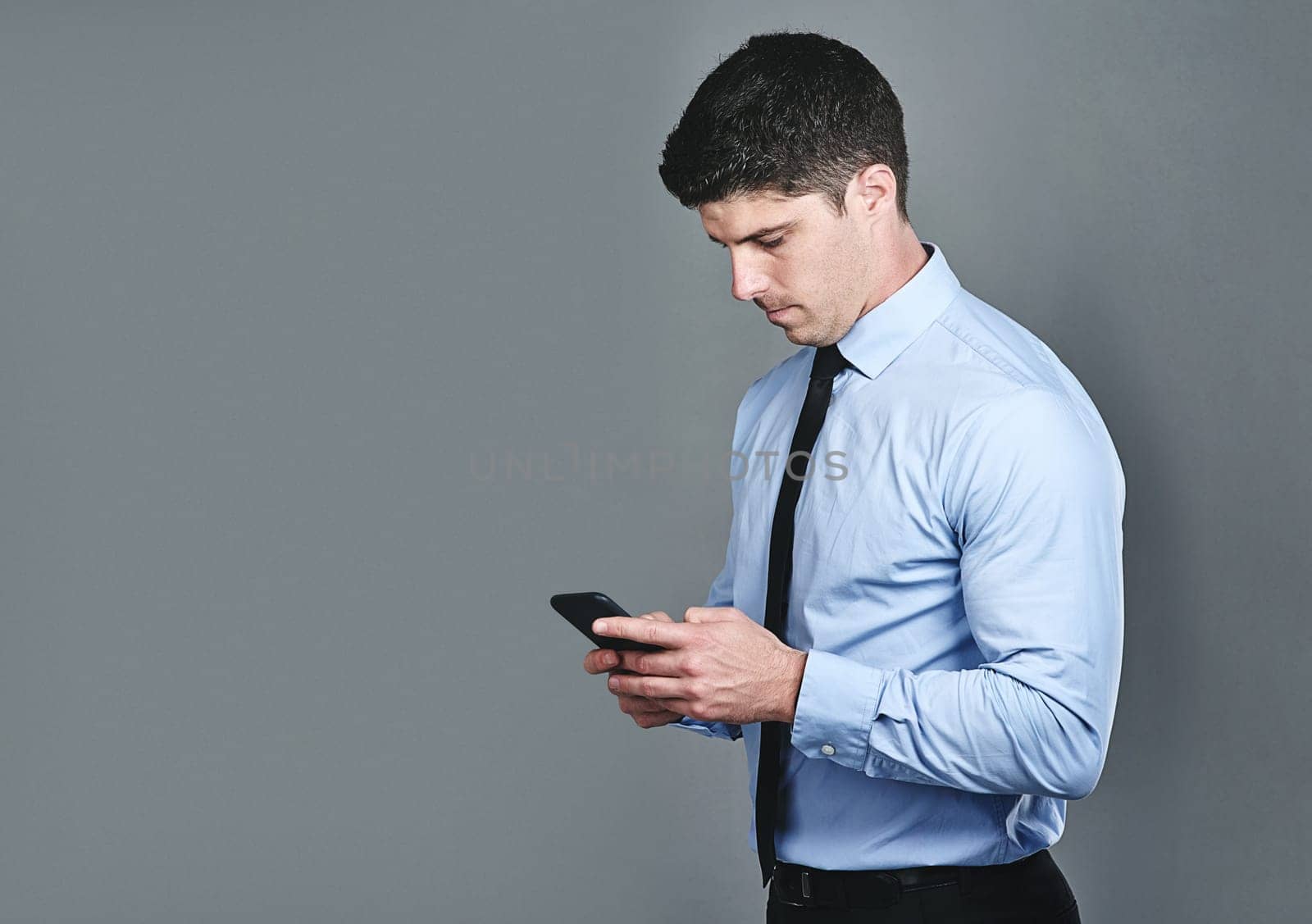 Its essential to maintain communication with clients. Studio shot of a young businessman texting on a cellphone against a grey background. by YuriArcurs