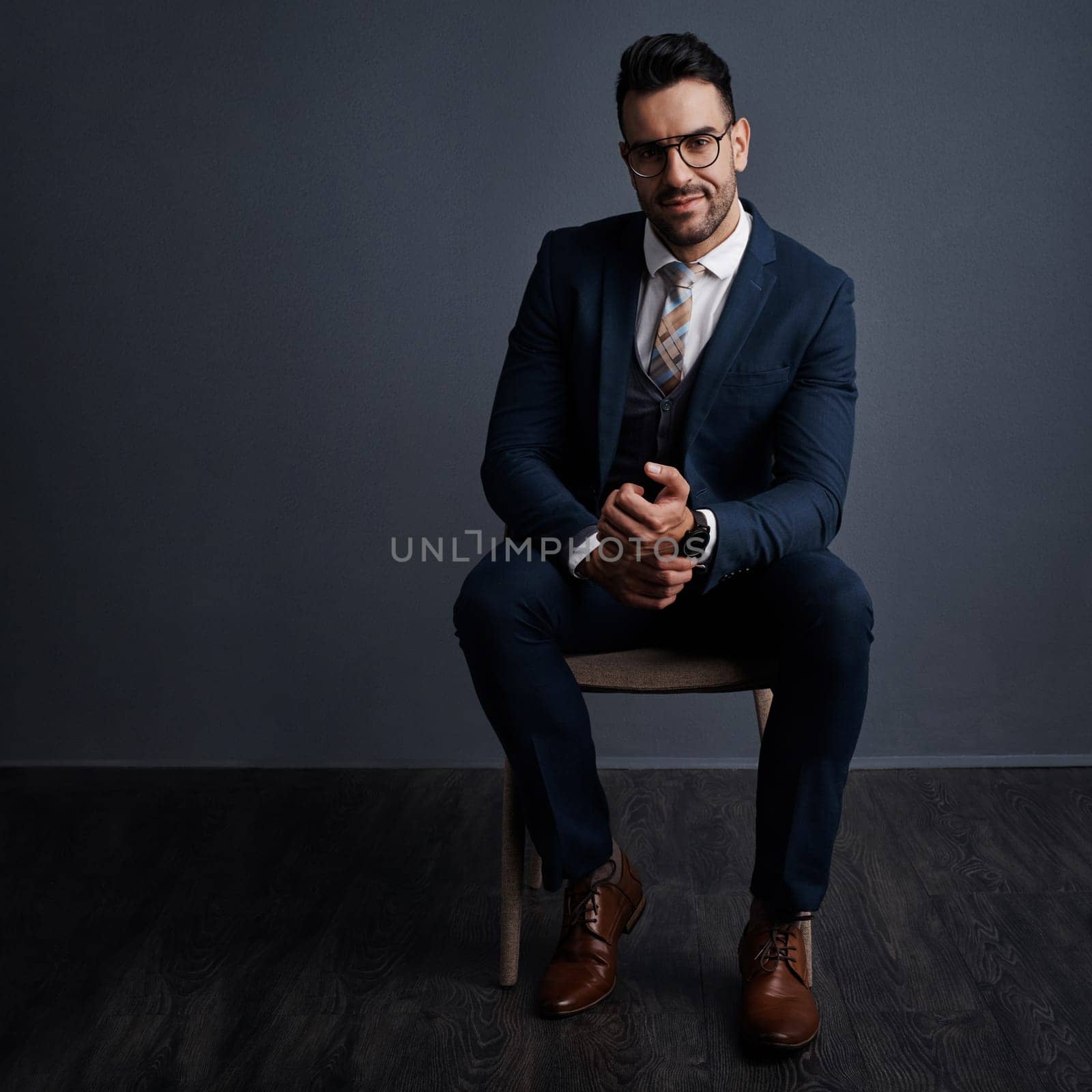 Style that inspires success. Studio shot of a stylish young businessman sitting on a chair against a gray background