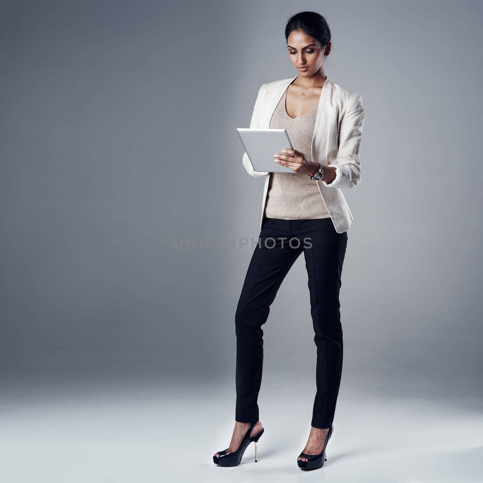Tracking business trends online. Studio shot of a young businesswoman using a digital tablet against a gray background. by YuriArcurs