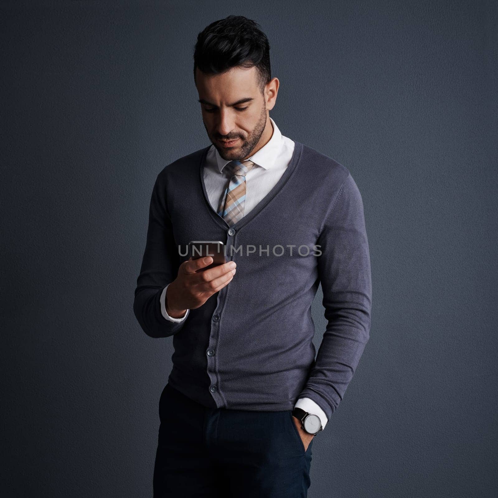 Getting work done in mobile format. Studio shot of a stylish young businessman using a mobile phone against a gray background. by YuriArcurs