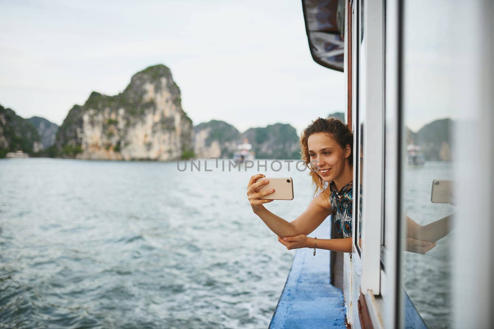 Life is a photo album full of memories. a young woman taking selfies on a boat ride in Vietnam with her smartphone. by YuriArcurs