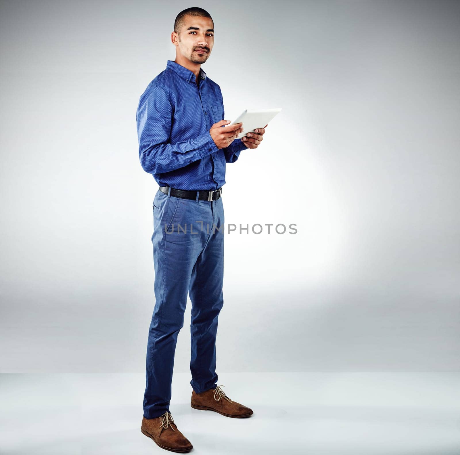Stay current or ahead of the game. Studio shot of a young businessman using his tablet against a grey background. by YuriArcurs