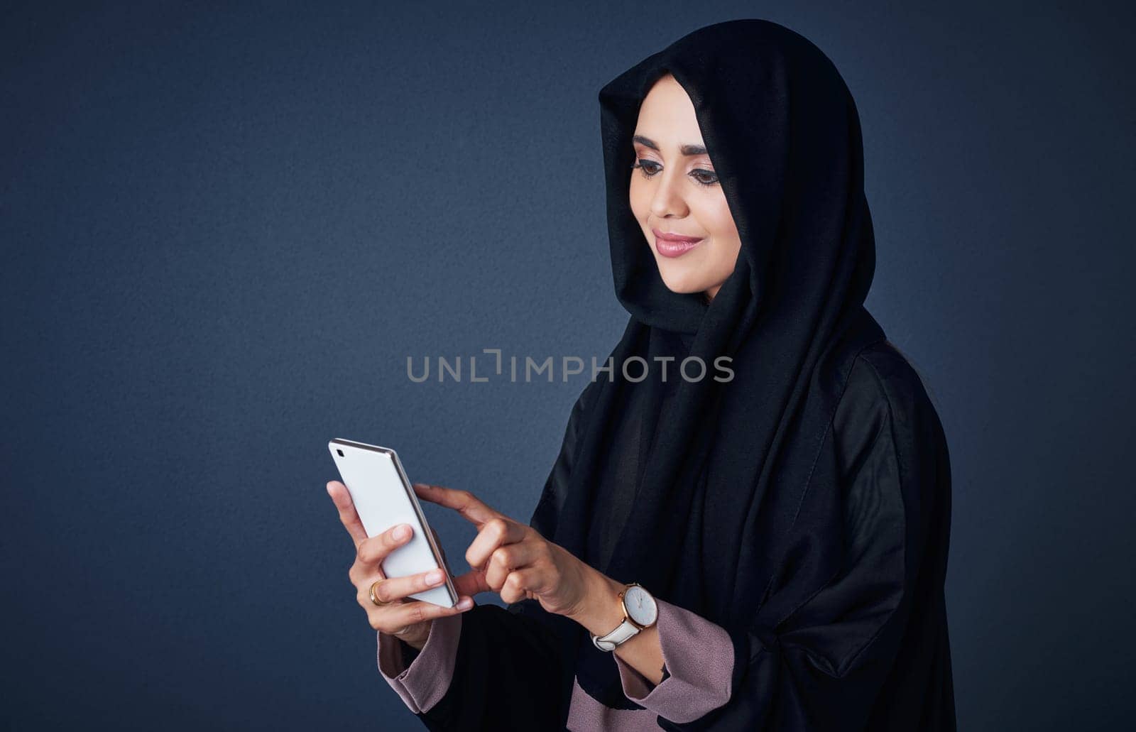 The smartest way of communication for her. Studio shot of a young woman wearing a burqa and using a mobile phone against a gray background. by YuriArcurs