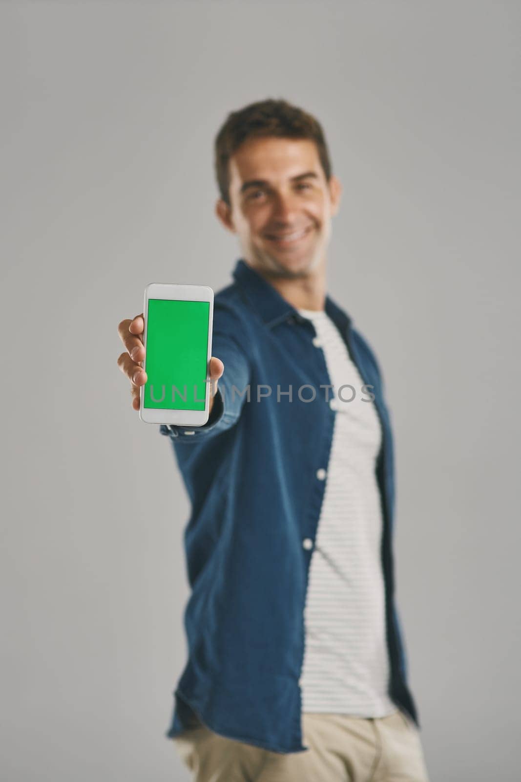 Living the smart life. Studio portrait of a young man holding a cellphone with a green screen against a grey background. by YuriArcurs