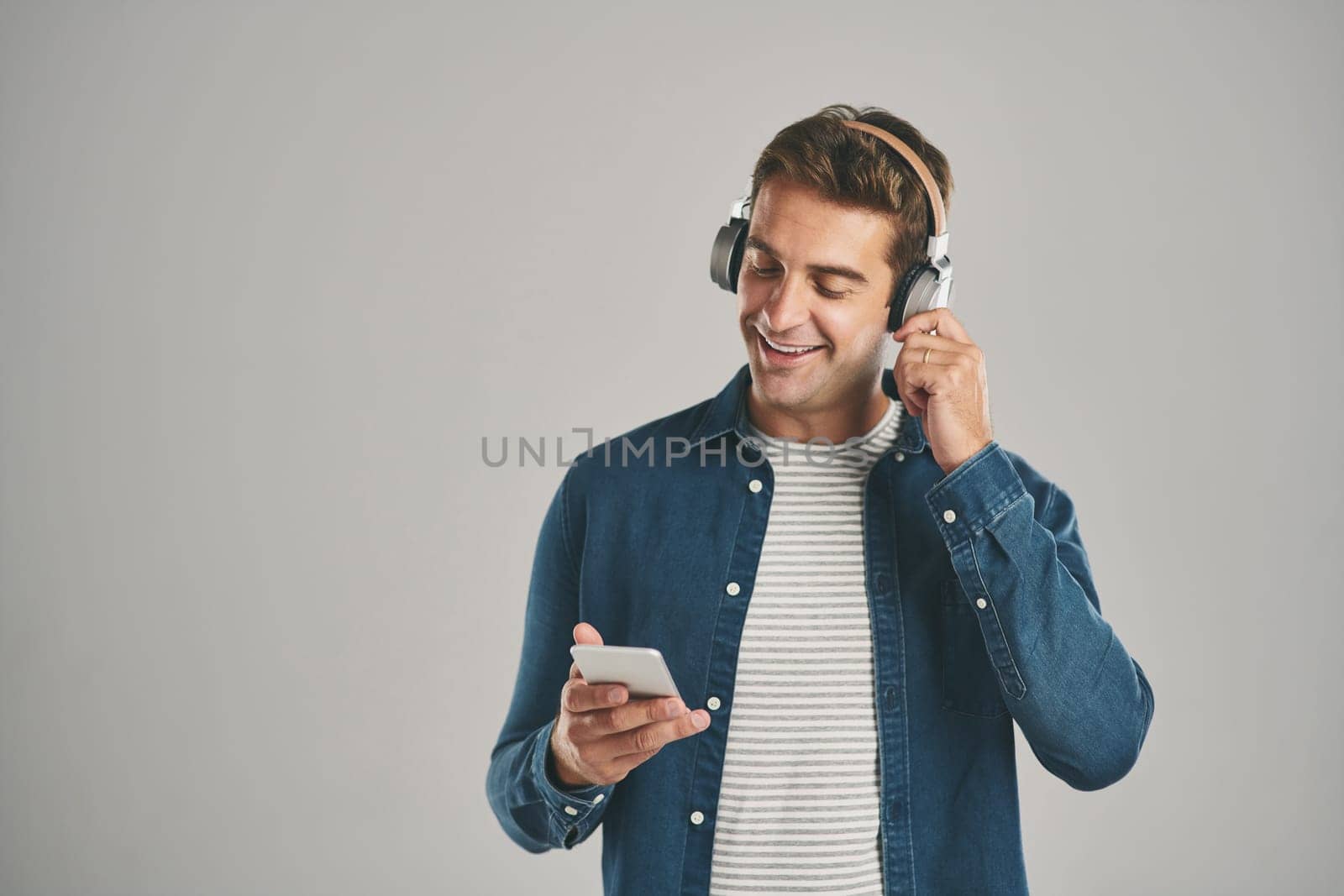 This music suits my taste. Studio shot of a young man using a cellphone while listening to music against a grey background