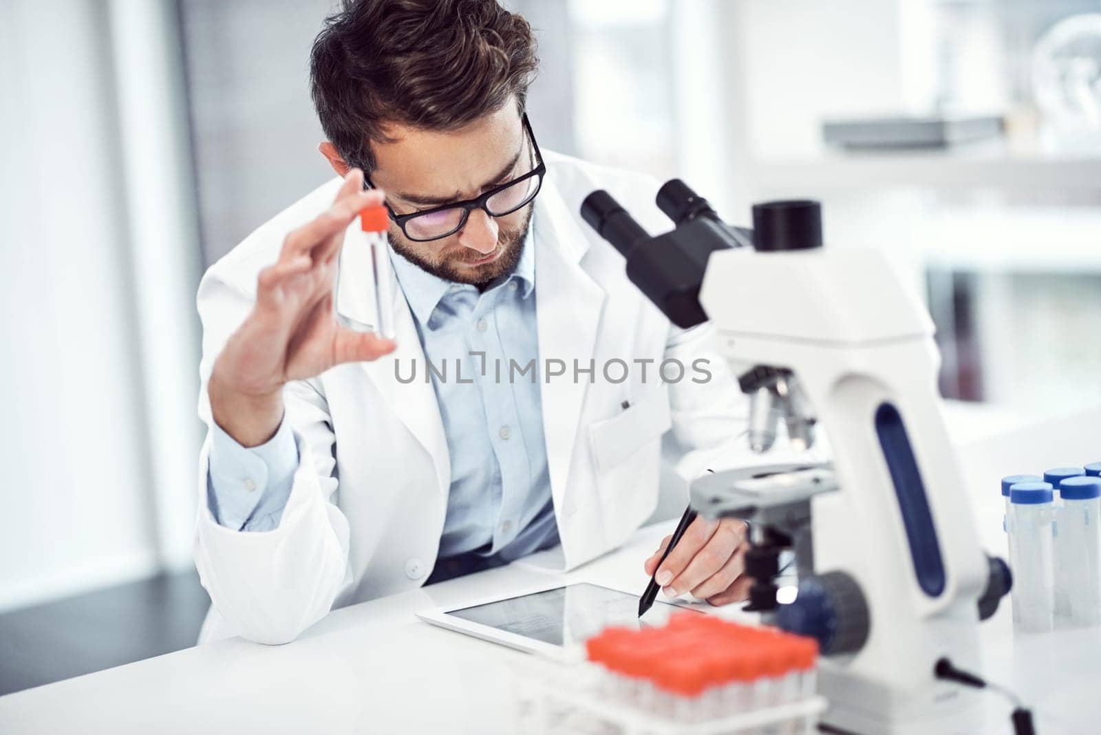 This is the very last vile. a focused young male scientist making notes while holding up a test tube inside of a laboratory