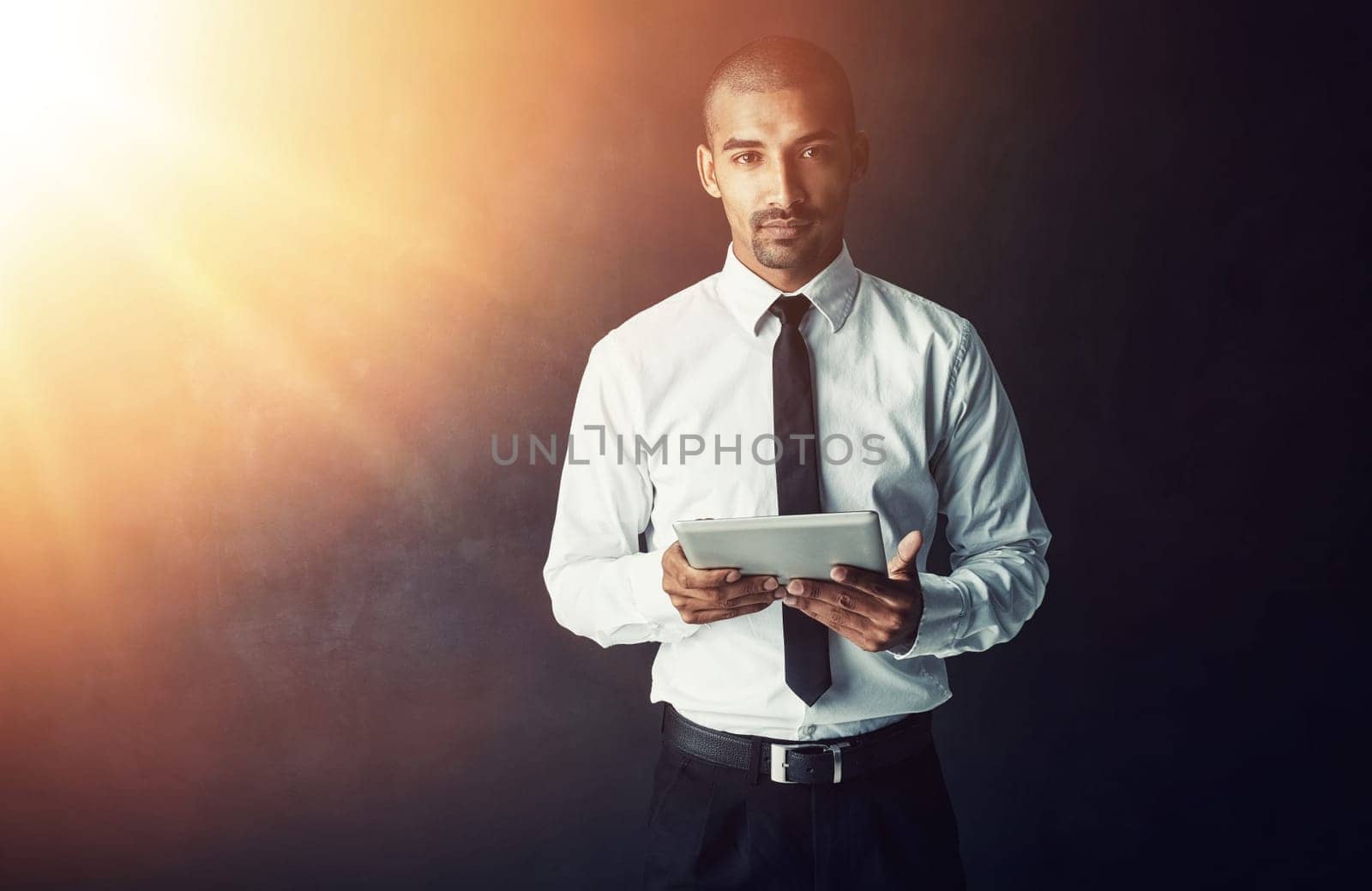 Modern business demands staying connected. Studio portrait of a young businessman using a digital tablet against a dark background