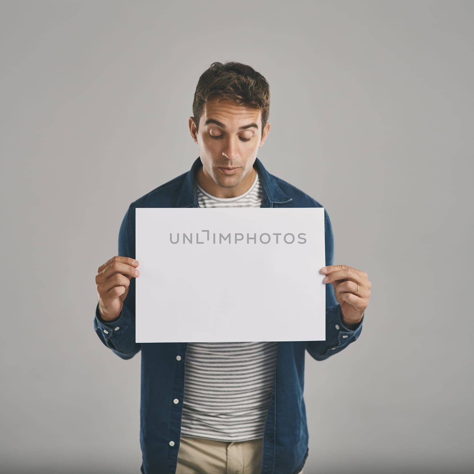 Ooh, what do we have here...Studio shot of a young man holding a blank placard against a grey background. by YuriArcurs