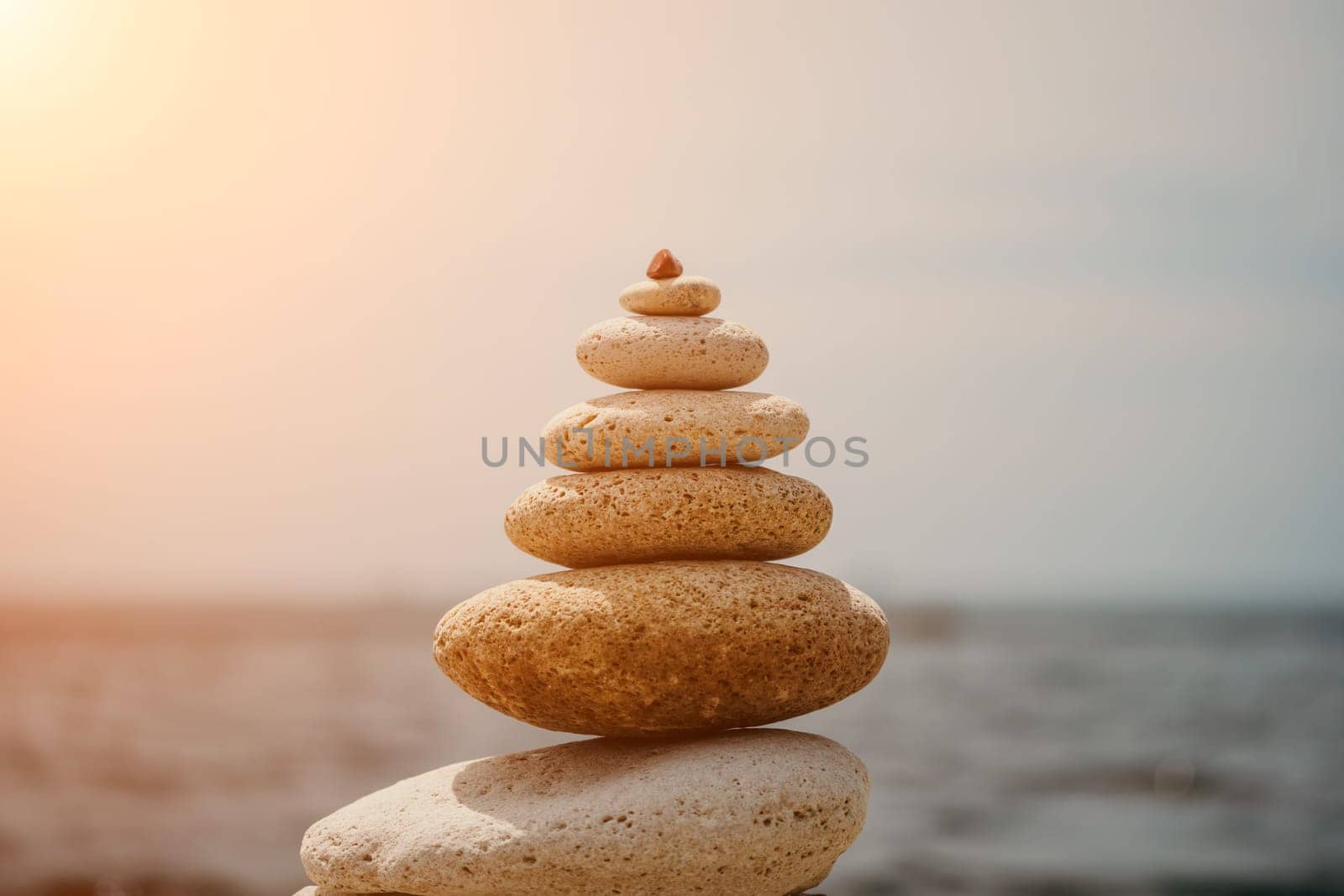 Pyramid stones on the seashore with warm sunset on the sea background. Happy holidays. Pebble beach, calm sea, travel destination. Concept of happy vacation on the sea, meditation, spa, calmness.