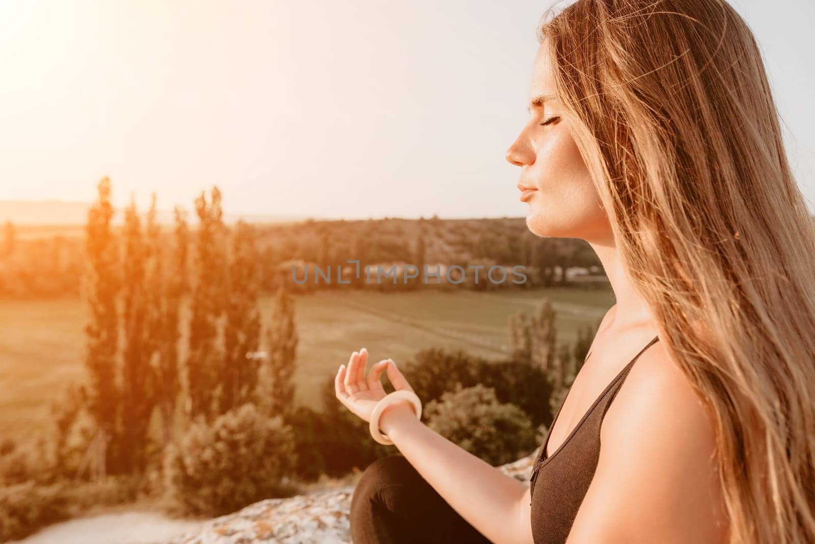 Well looking middle aged woman with long hair, fitness instructor in leggings and tops doing stretching and pilates on the rock near forest. Female fitness yoga routine concept. Healthy lifestyle.