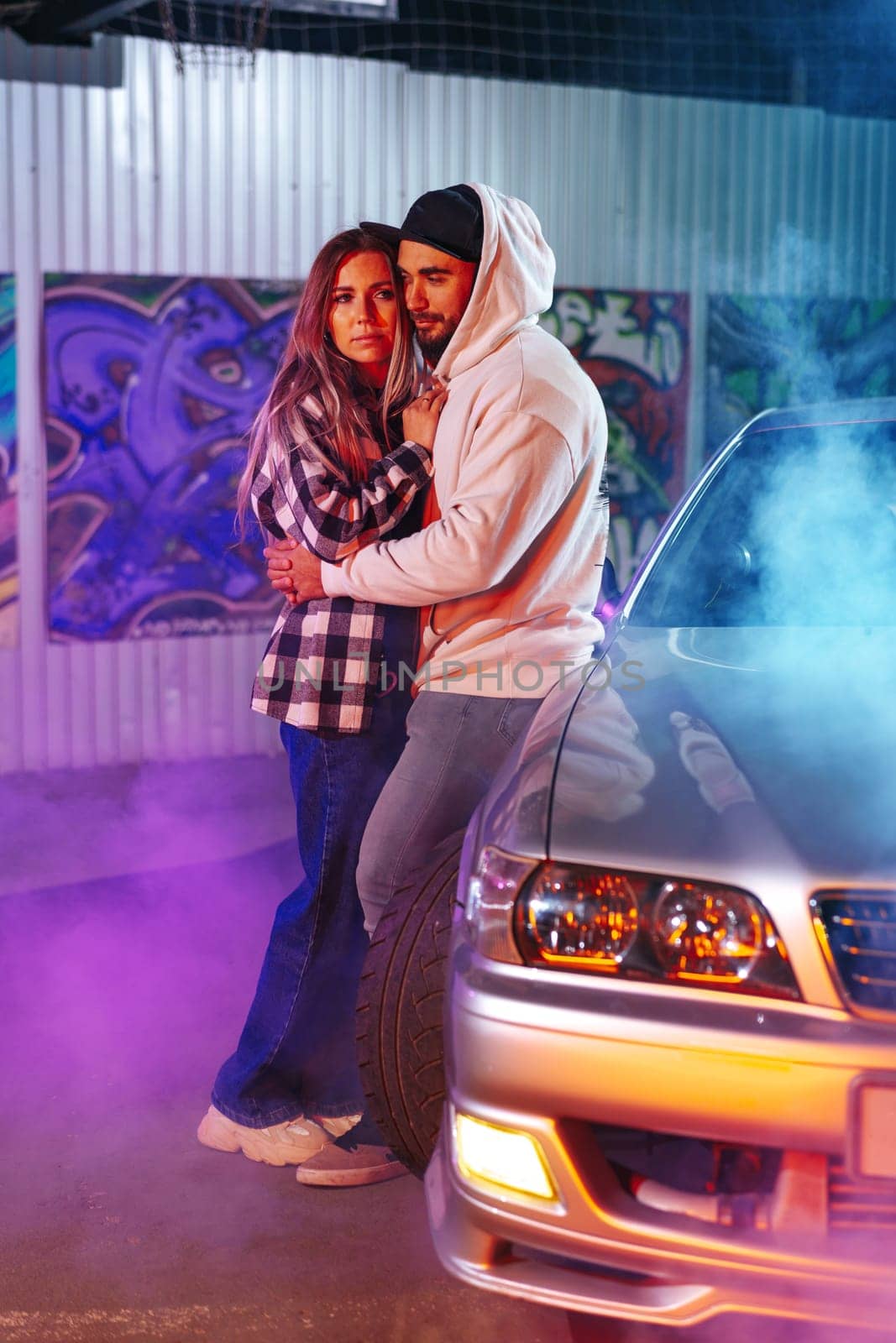 Smiling loving couple standing near sport car over night city background