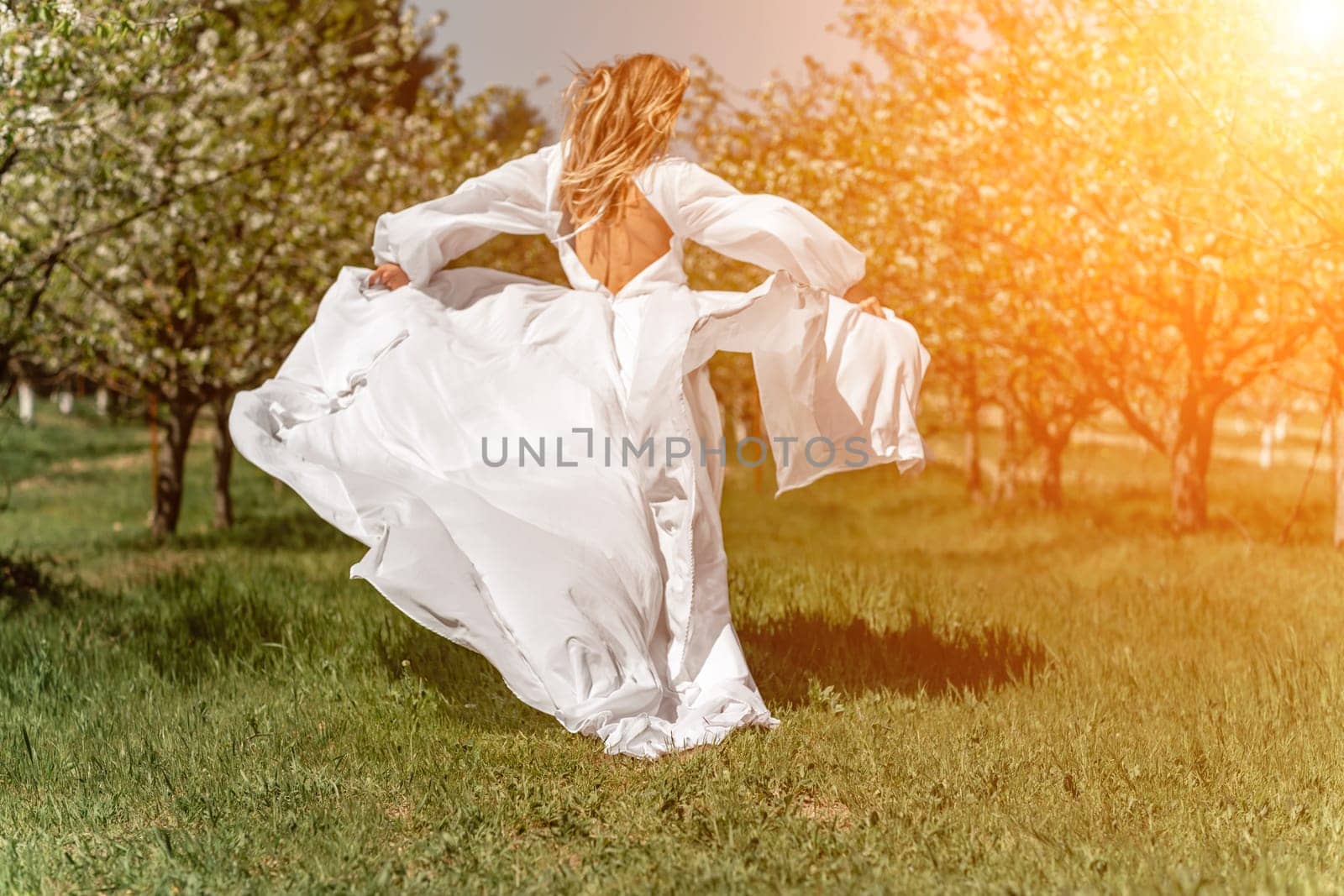 Woman white dress park. A woman in a white dress runs through a blossoming cherry orchard. The long dress flies to the sides, the bride runs rejoicing in life. by Matiunina