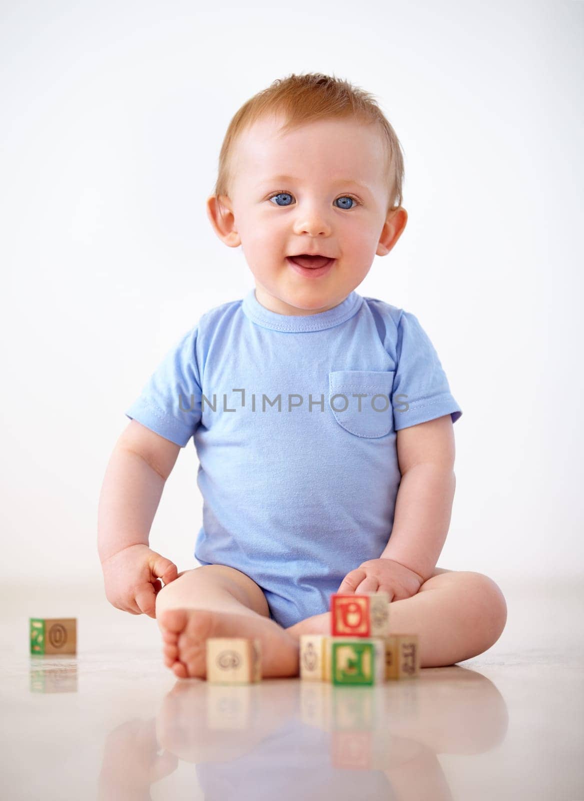 Happy, baby with toy blocks and playing against a white background with smile. Child development or learning, happiness or health wellness and boy toddler play against a studio backdrop on floor.