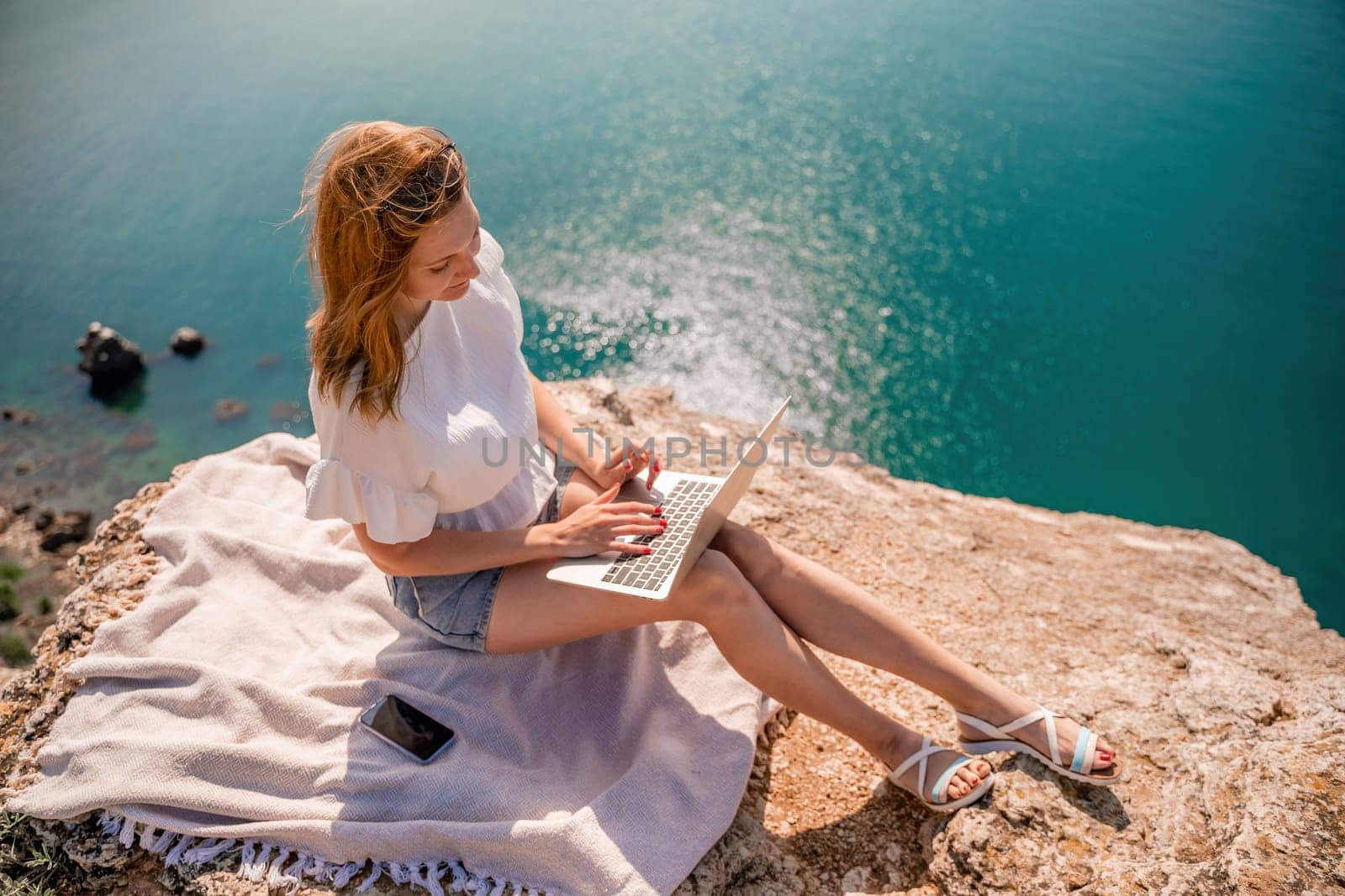 Freelance woman working on a laptop by the sea, typing away on the keyboard while enjoying the beautiful view, highlighting the idea of remote work. by Matiunina