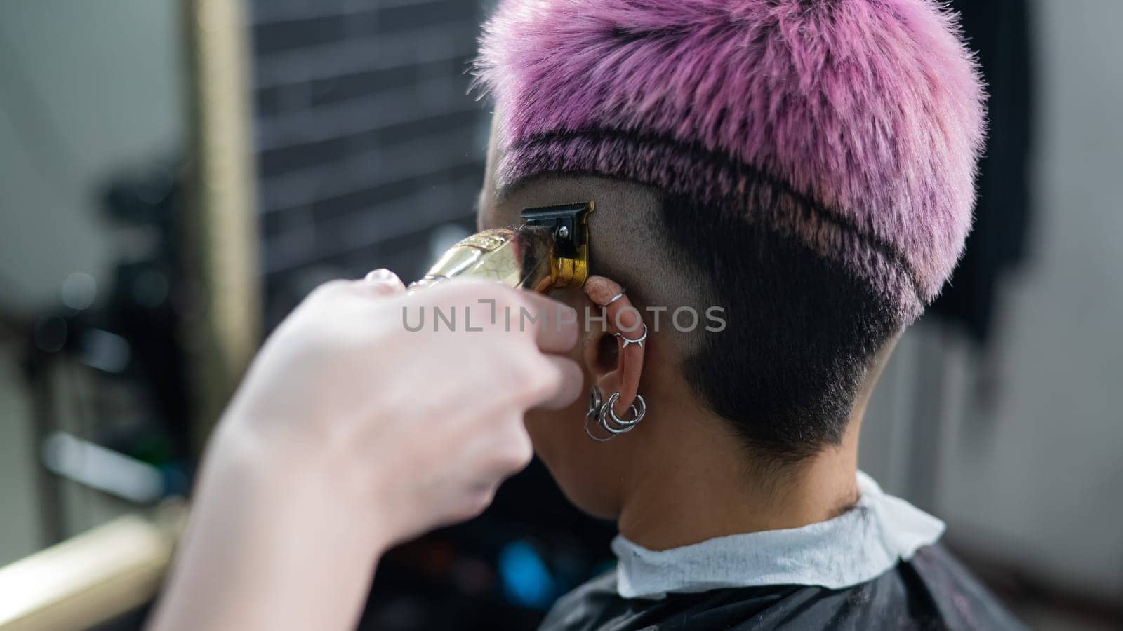 The hairdresser shaves the temple of a female client. Rear view of a woman with short pink hair in a barbershop. by mrwed54