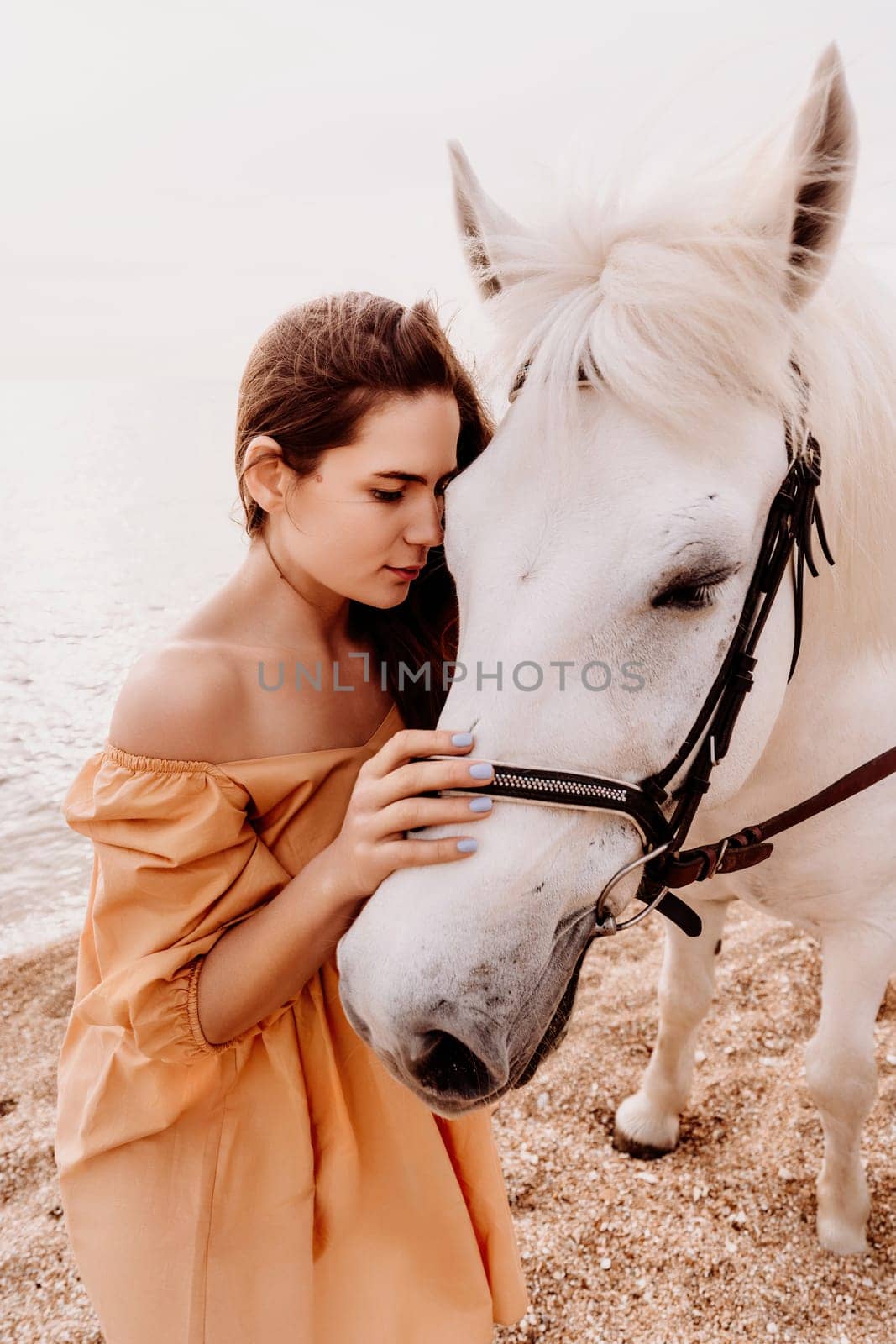 A white horse and a woman in a dress stand on a beach, with the sky and sea creating a picturesque backdrop for the scene. by Matiunina
