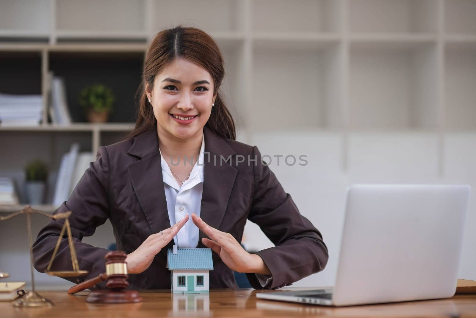 Asian businesswoman lawyer sitting at the office holding a pen taking note working on a loan a sample home mallet a laptop at the table. by wichayada