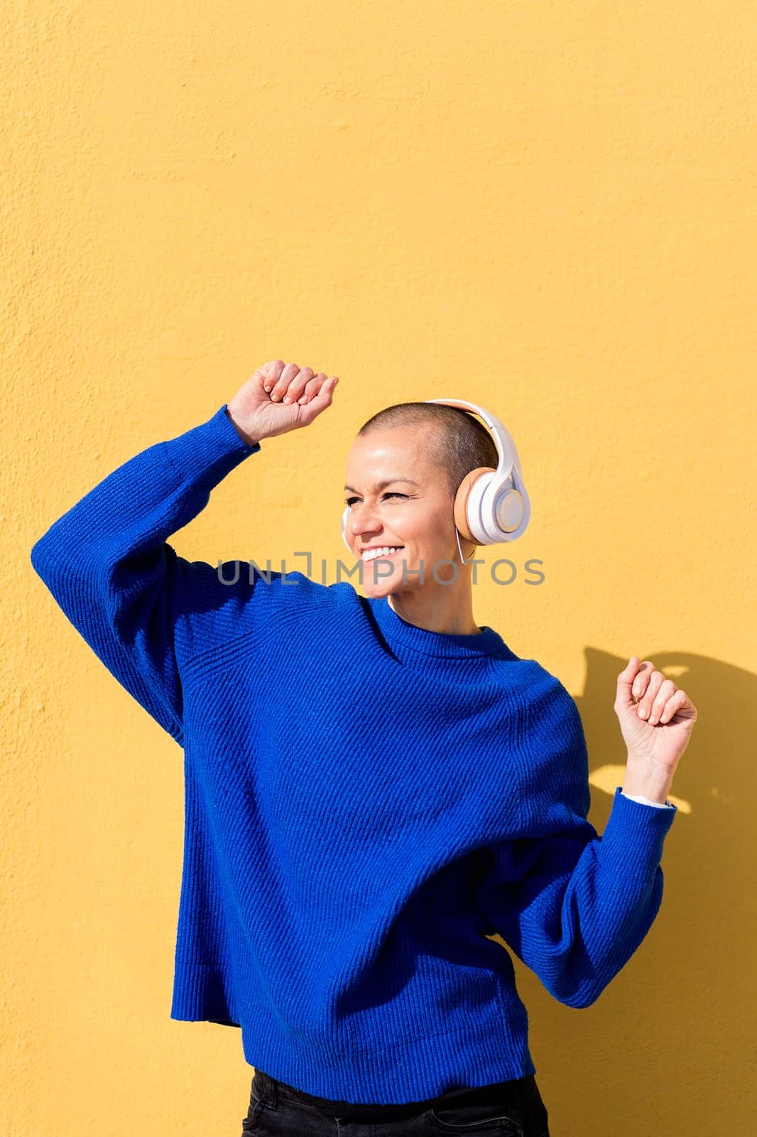 woman smiling happy while dancing listening to music in headphones with a yellow wall in the background, concept of rhythm and positive people, copy space for text