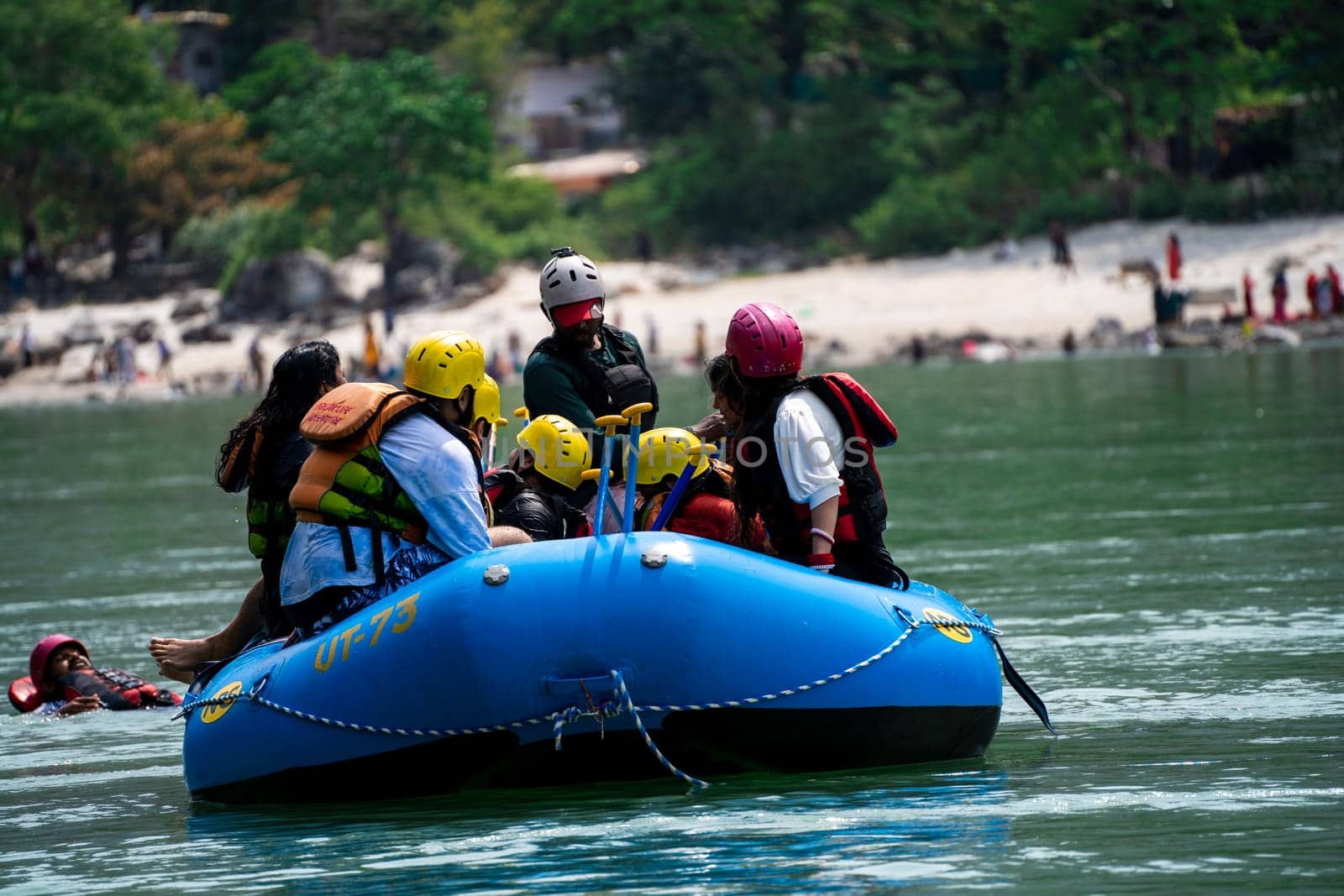 Rishikesh, Haridwar, India - circa 2023: family friends sitting in raft enjoying adventure sports while crossing in front of ghat and temple on the banks of the holy river ganga