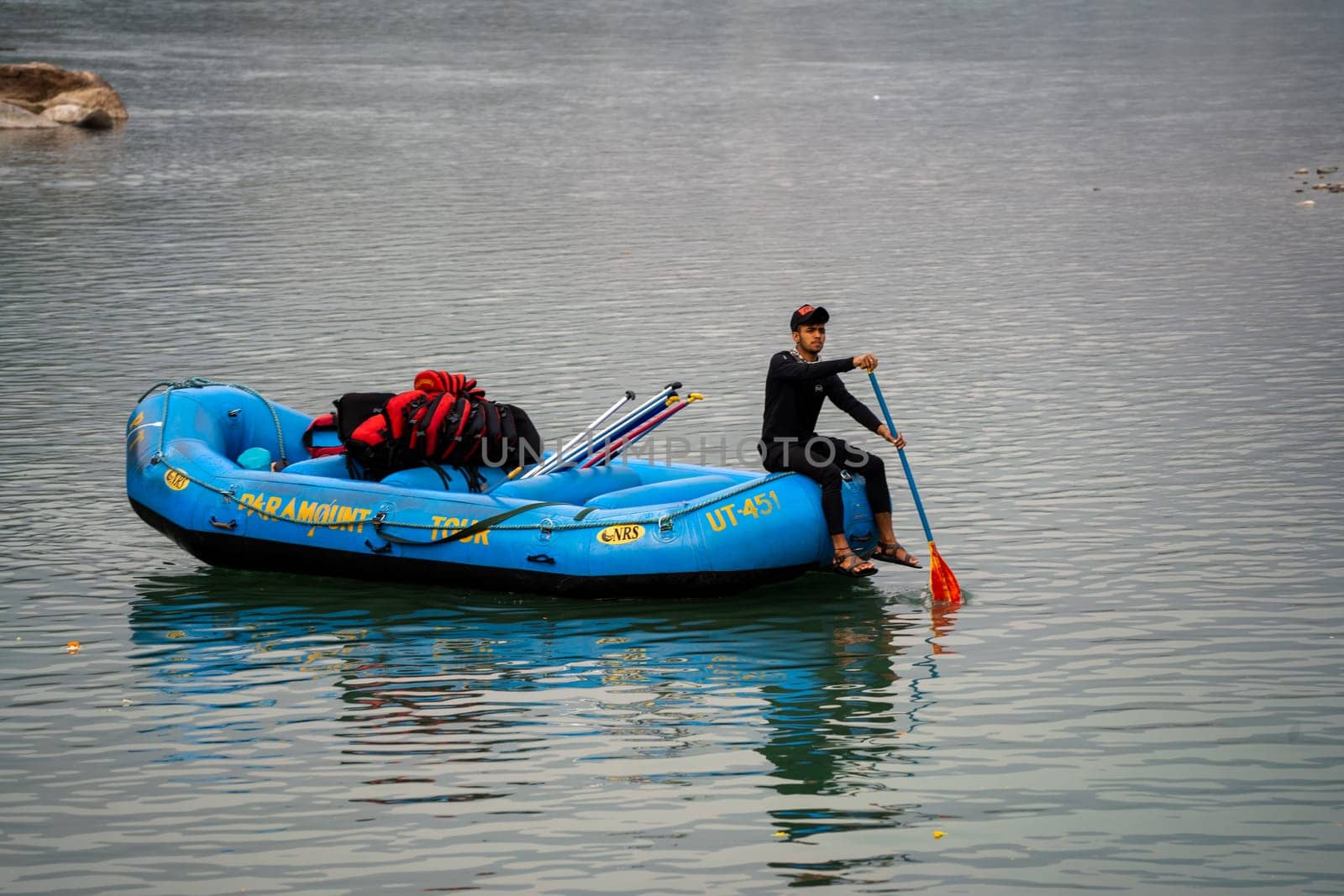 Rishikesh, Haridwar, India - circa 2023: man in black enjoying solo ride on inflatable white water raft while transporting life jackets and waiting for people to board for popular summer adventure sport