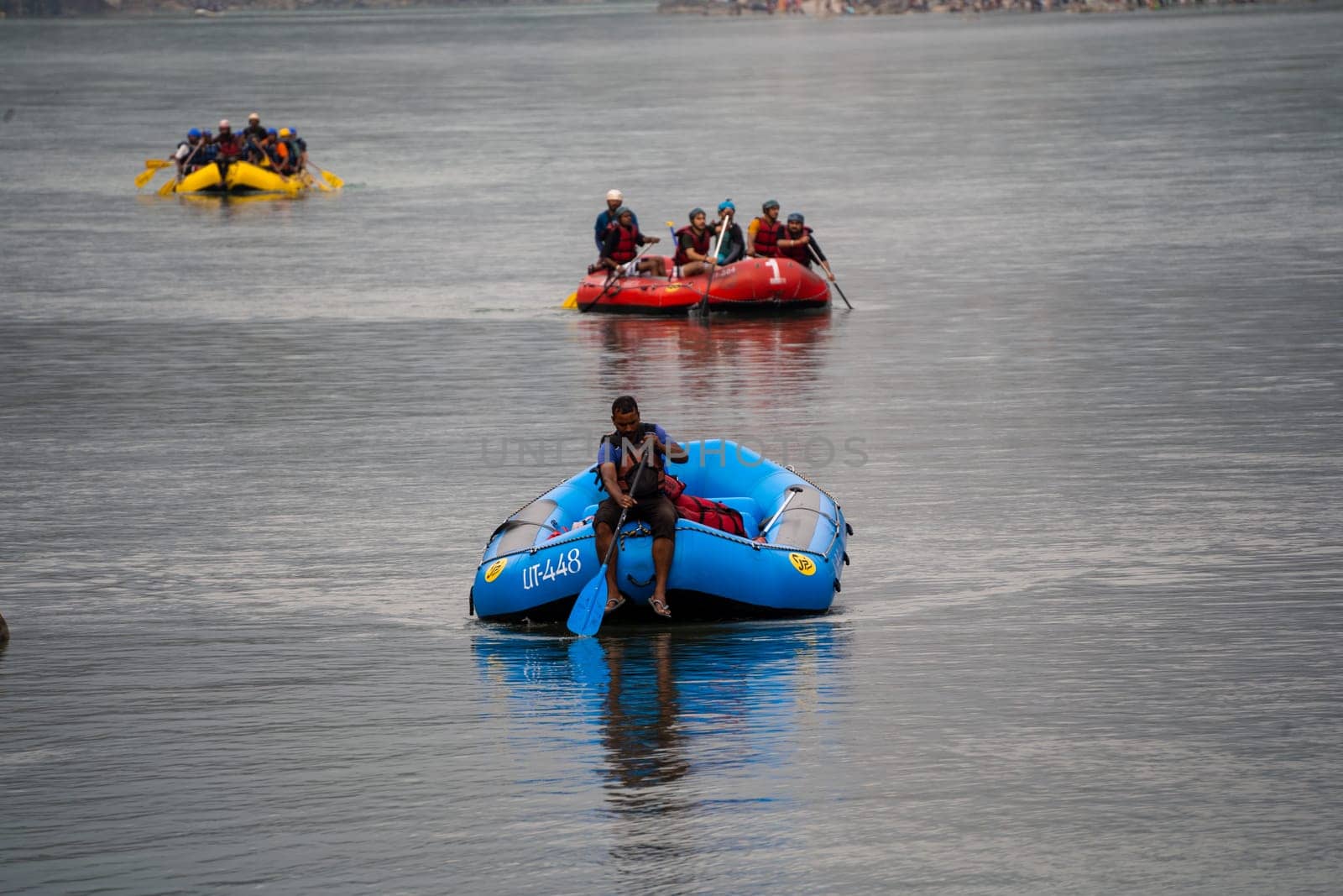 Rishikesh, Haridwar, India - circa 2023: man in black enjoying solo ride on inflatable white water raft while transporting life jackets and waiting for people to board for popular summer adventure sport