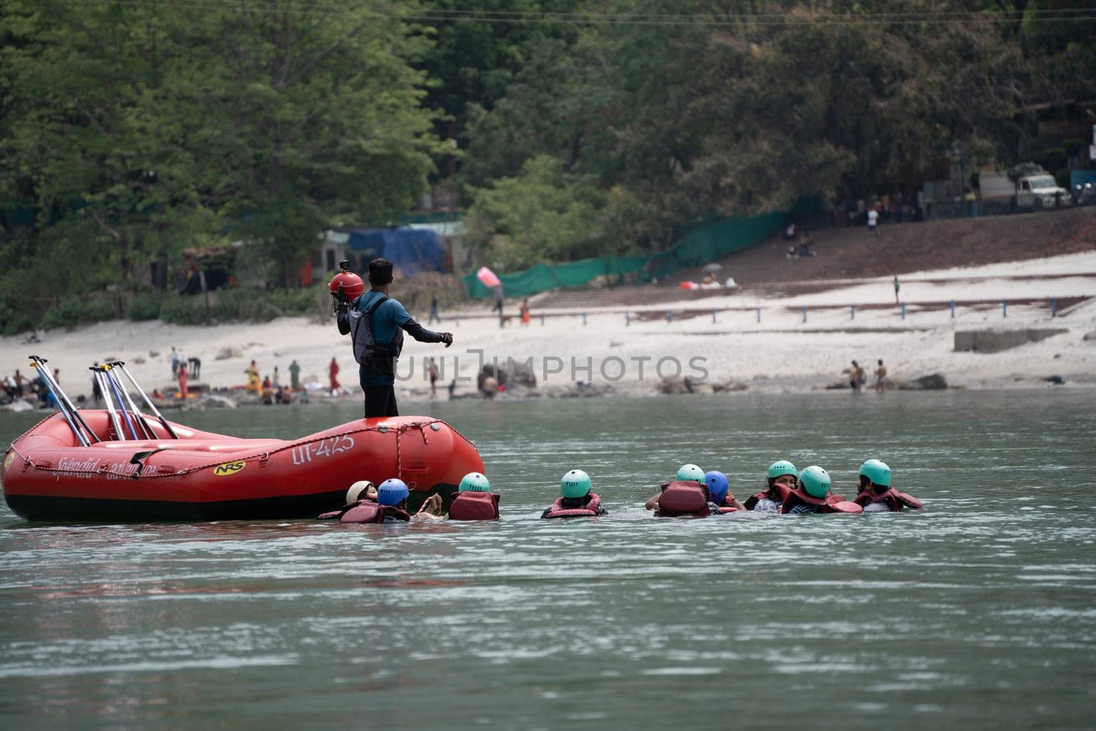 Rishikesh, Haridwar, India - circa 2023: group of people, friends, family floating in blue green cool water of ganga near an inflatable raft and being pulled into it a popular adventure sport