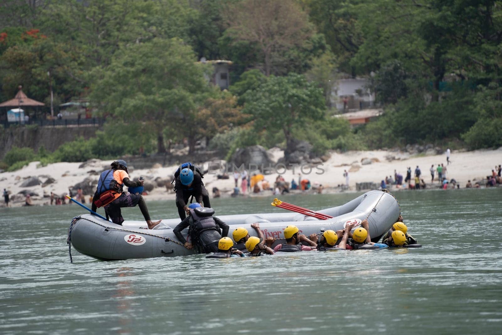 Rishikesh, Haridwar, India - circa 2023: group of people, friends, family floating in blue green cool water of ganga near an inflatable raft and being pulled into it a popular adventure sport