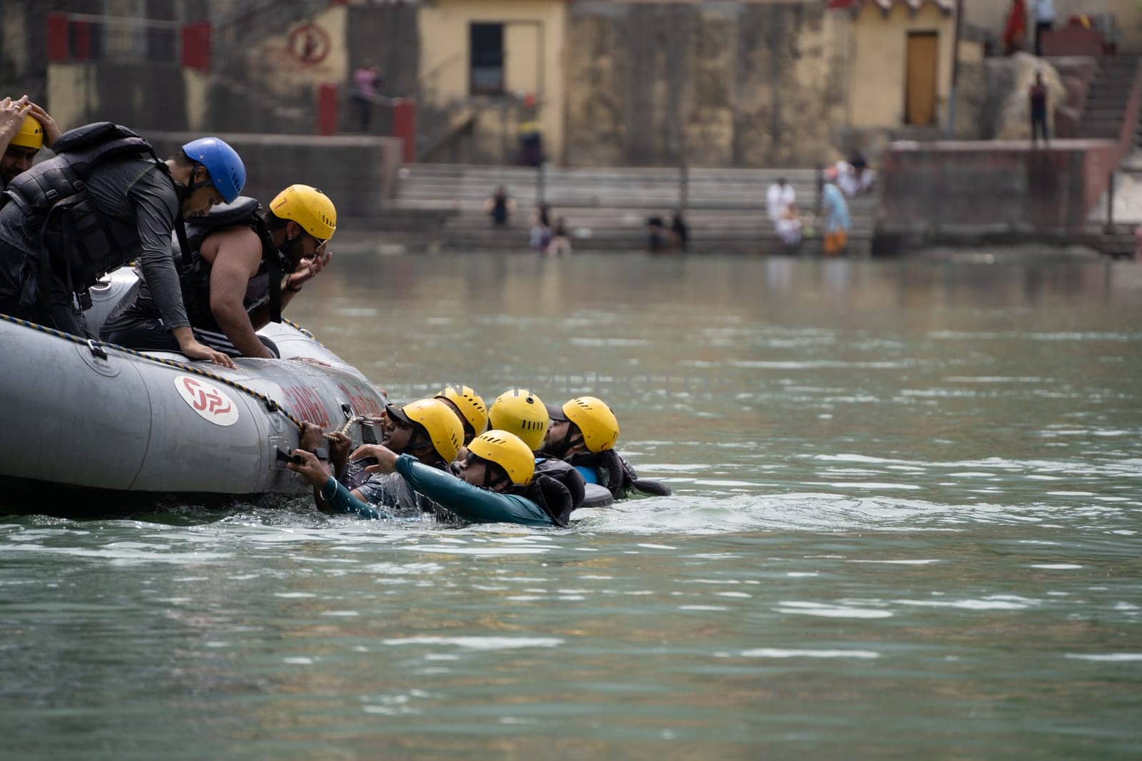 Rishikesh, Haridwar, India - circa 2023: group of people, friends, family floating in blue green cool water of ganga near an inflatable raft and being pulled into it a popular adventure sport