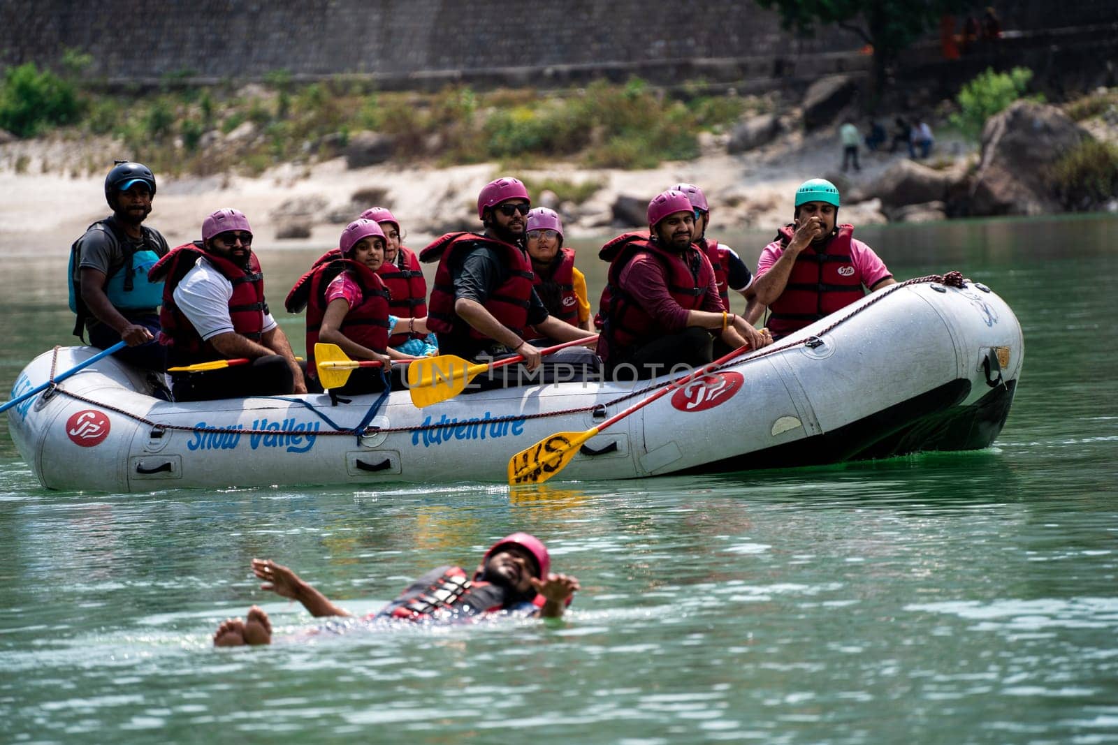 Rishikesh, Haridwar, India - circa 2023: group of people, friends, family floating in blue green cool water of ganga near an inflatable raft and being pulled into it a popular adventure sport