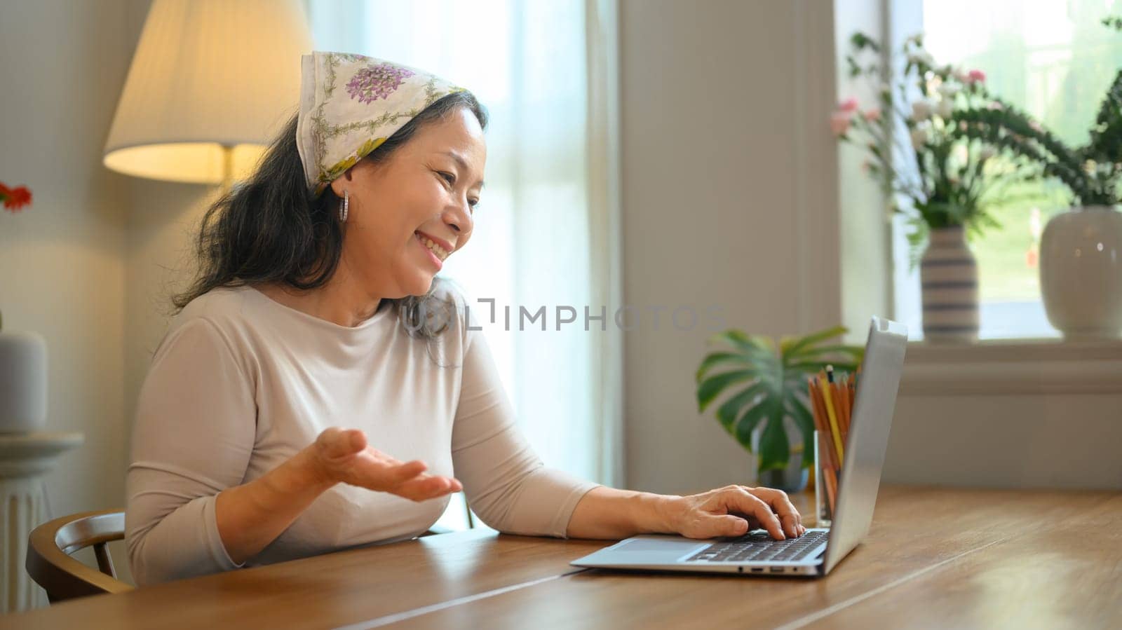 Positive stylish middle age woman having video call with family or friends on laptop. People, technology and communication concept.
