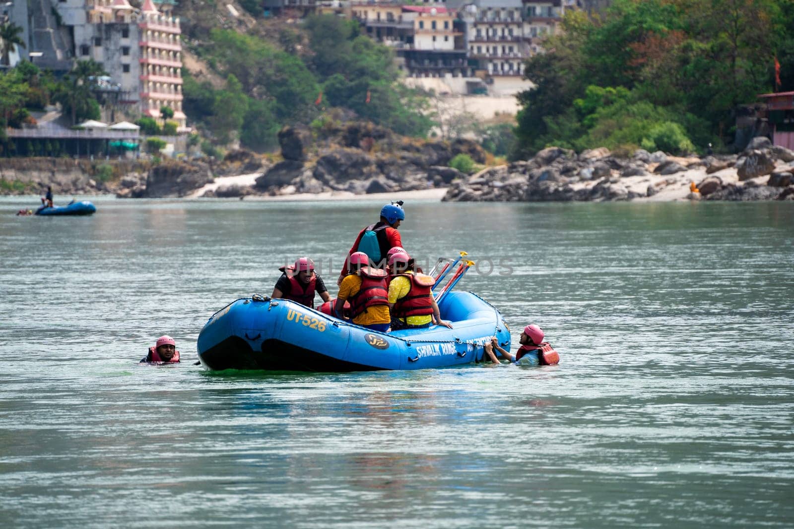 Rishikesh, Haridwar, India - circa 2023: group of people, friends, family floating in blue green cool water of ganga near an inflatable raft and being pulled into it a popular adventure sport