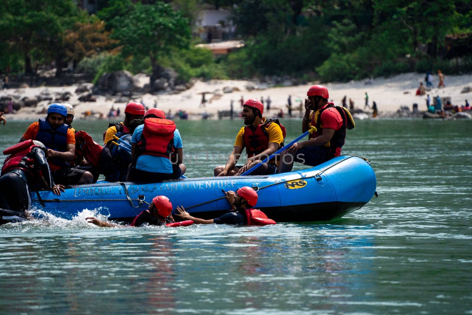 Rishikesh, Haridwar, India - circa 2023: group of people, friends, family floating in blue green cool water of ganga near an inflatable raft and being pulled into it a popular adventure sport