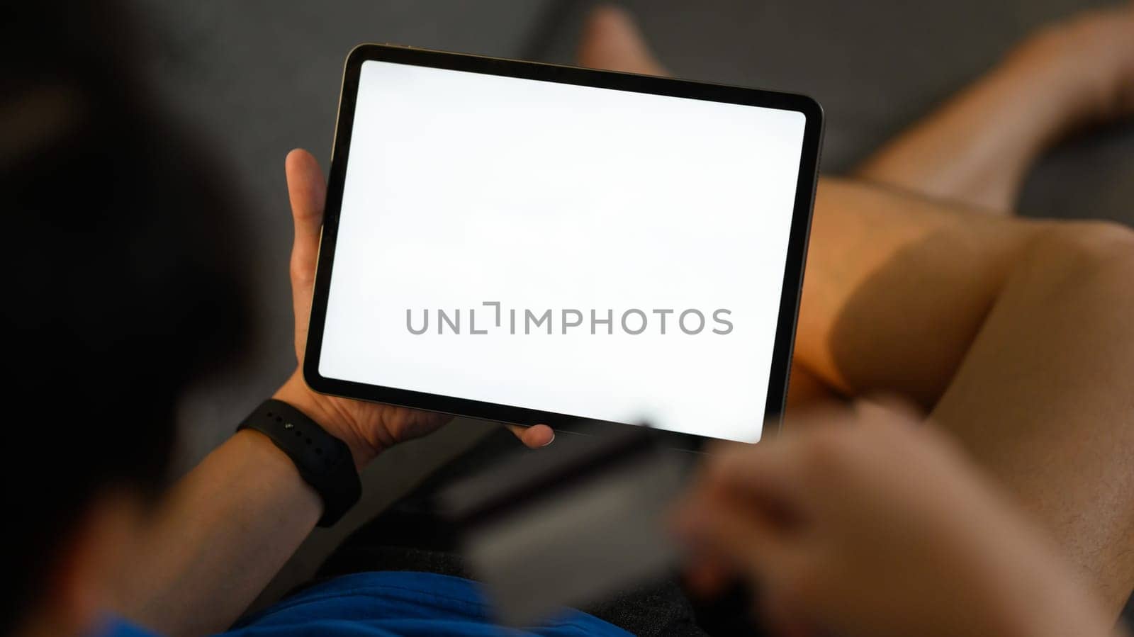 Closeup shot of casual man lying on couch and using digital tablet. White empty screen for advertise text.