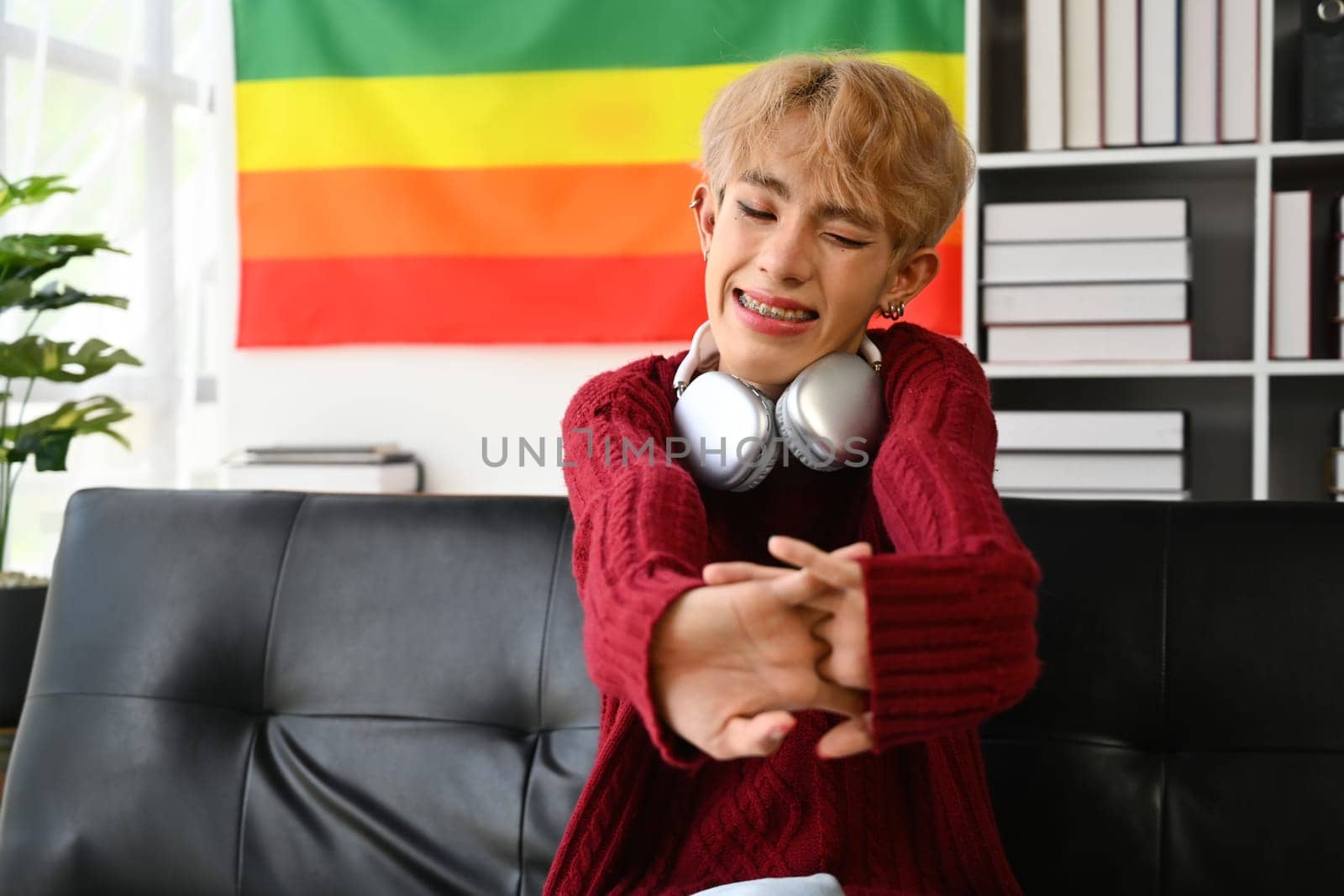 Happy teenage gay man enjoying weekend and relaxing on comfortable couch at home. LGBTQ, people lifestyle, leisure concept.