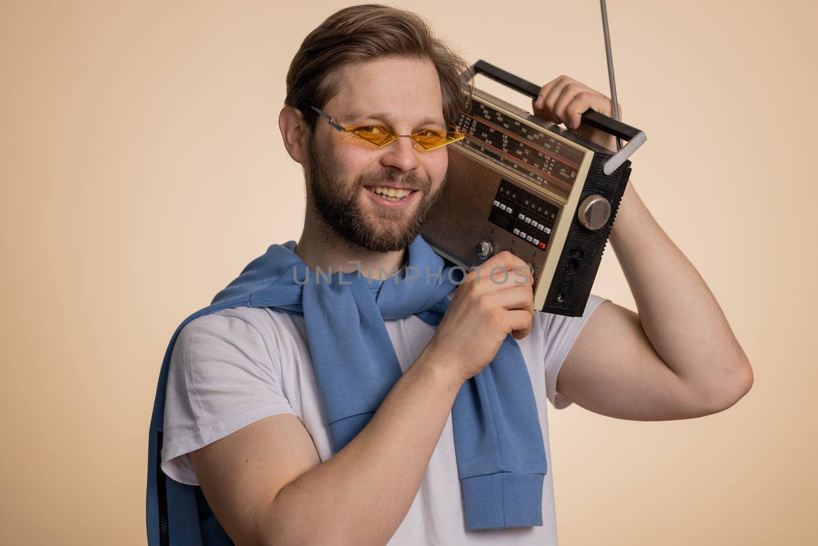 Happy Caucasian man using retro tape record player to listen music, disco dancing of favorite track, having fun, entertaining, fan of vintage technologies. Handsome guy isolated on beige background