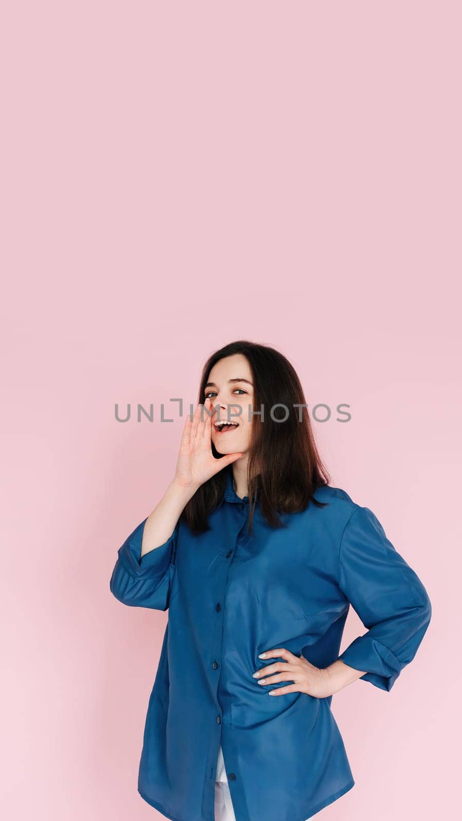 Excited Girl Sharing Breaking News: Hand Near Open Mouth Conveying Surprise and Delivering Important Information in an Empty Space, Isolated on a Pink Background.