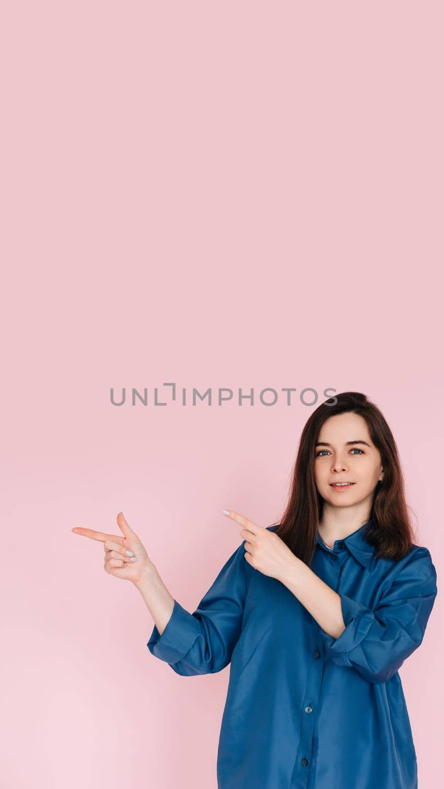 Cheerful Woman Pointing with Fingers at Empty Space, Conveying Information: Vibrant Photo on Pink Background.