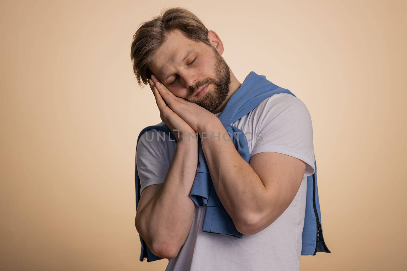 Tired overworked young caucasian man yawning, sleepy inattentive feeling somnolent lazy bored gaping suffering from lack of sleep. Handsome exhausted guy isolated on studio beige background indoor