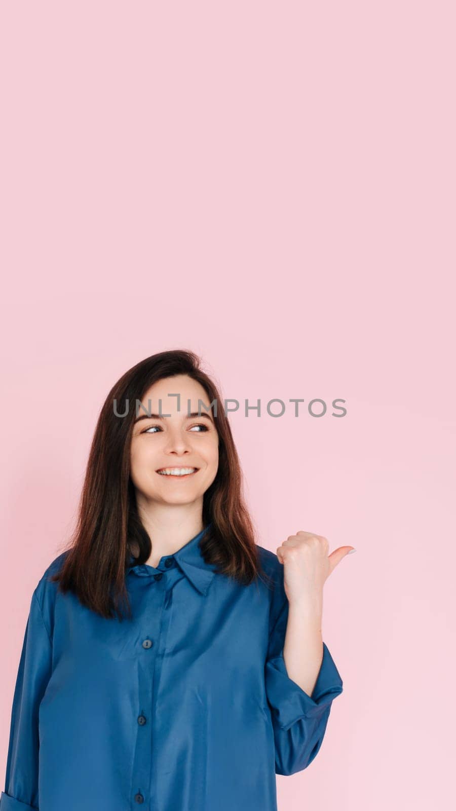 Radiant Portrait of Beautiful Woman with Joyful Smile, Pointing Finger and Looking at Empty Space, Isolated on Pink Background - News and Excitement Concept.