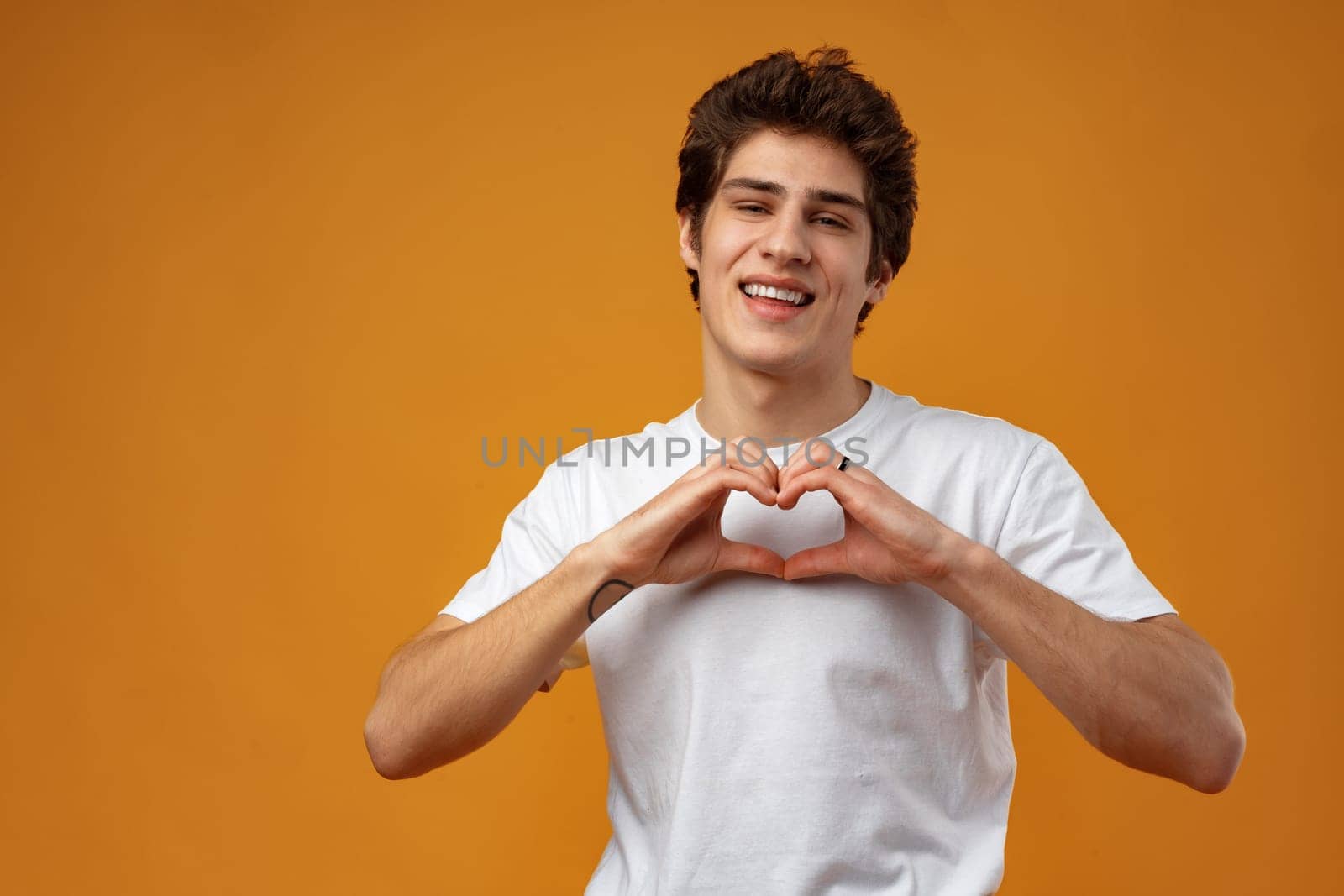 Portrait of happy handsome man making heart with fingers on yellow