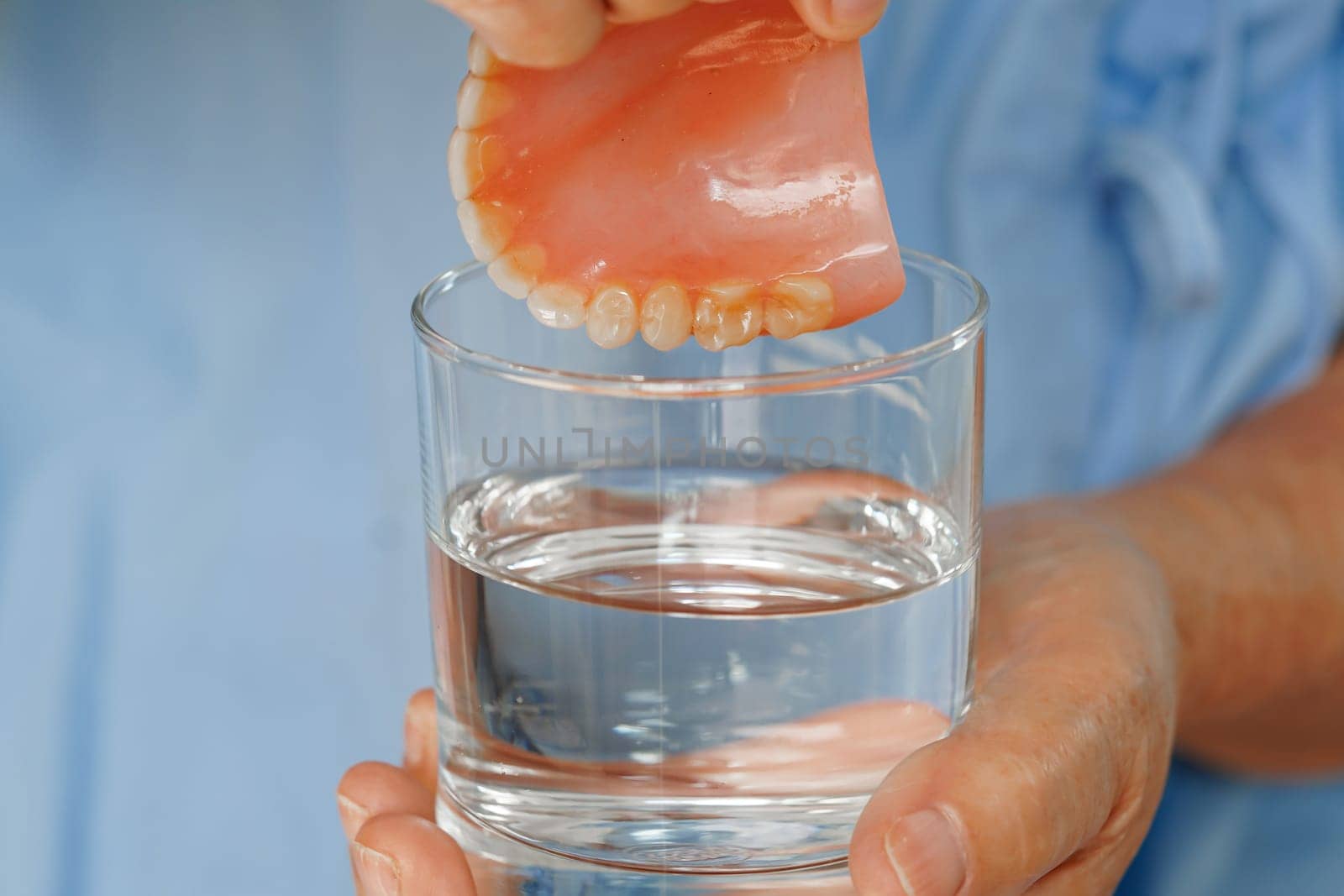 Asian senior woman patient clean teeth denture in a glass with solution for chew food. by sweettomato