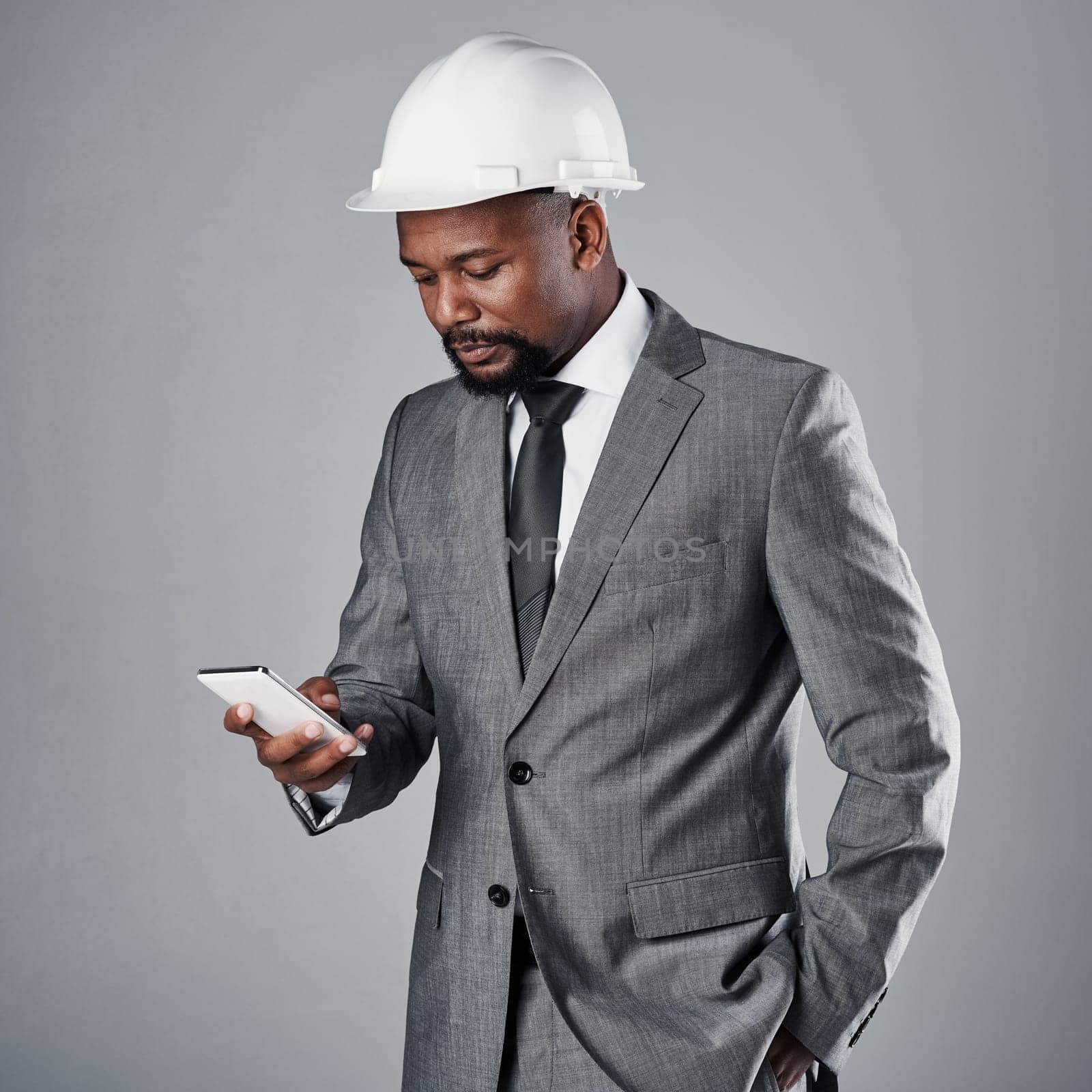 His team can always reach him. a well-dressed civil engineer using his cellphone while standing in the studio