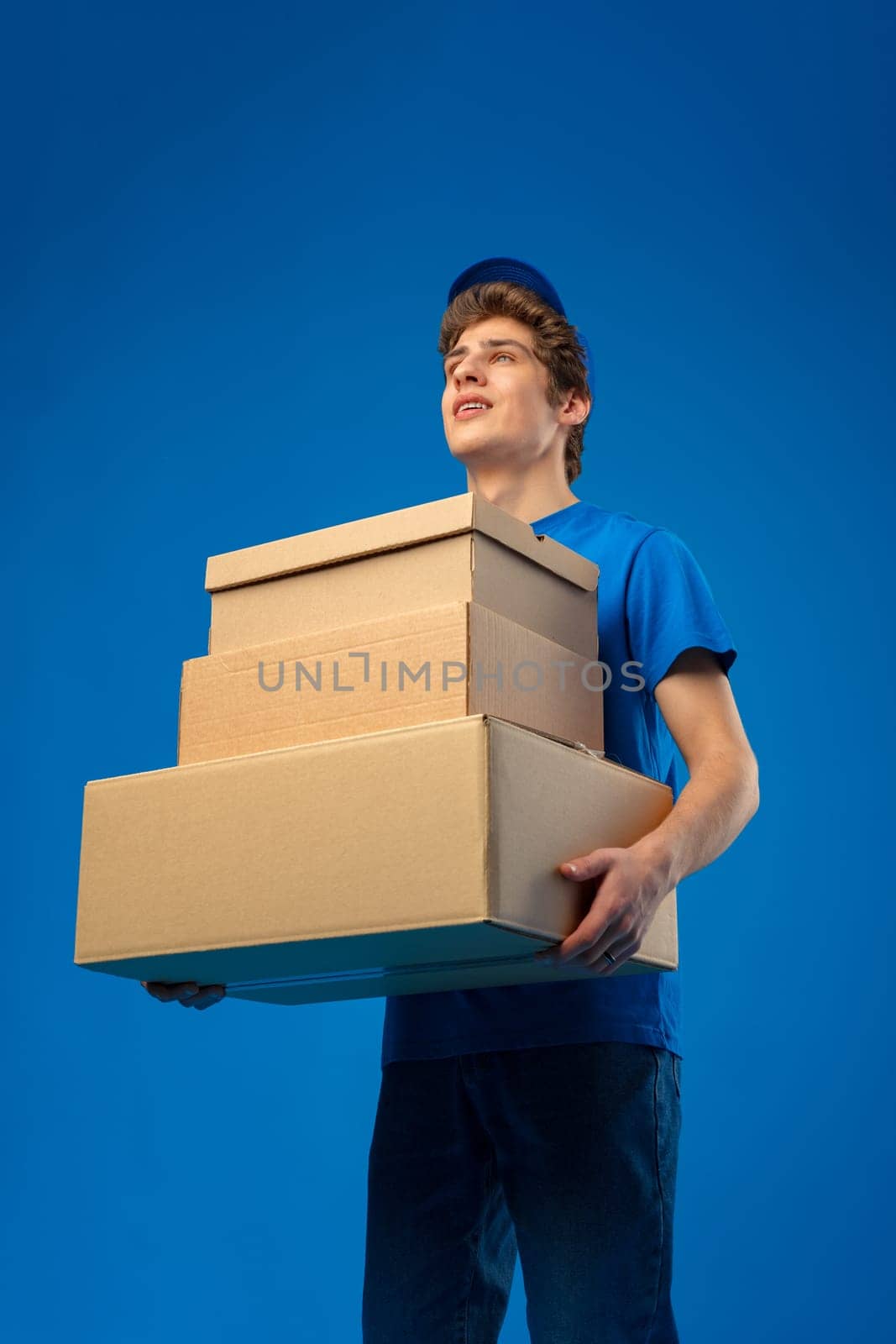 Young male courier in a blue uniform holds parcel in his hands in studio