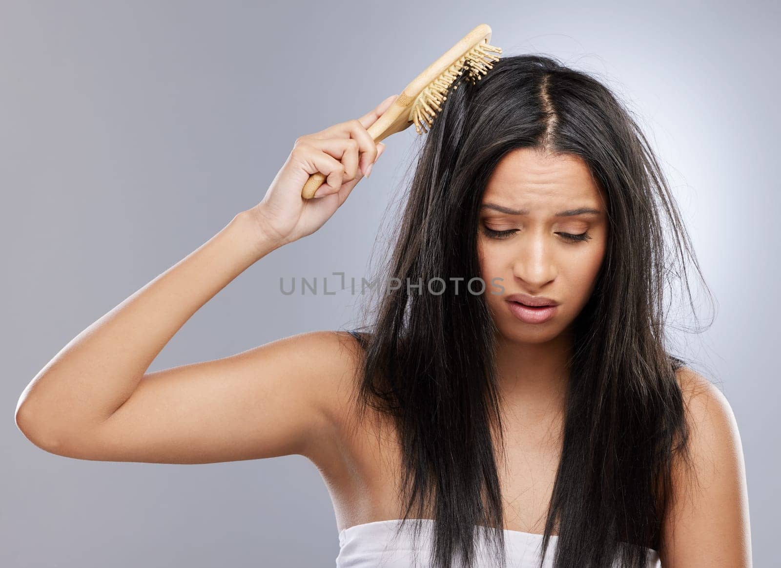 Hair, knot and woman with brush in studio with worry for split ends, haircare crisis and messy style. Beauty, hairdresser and female person with frizz, texture and tangle problem on gray background.
