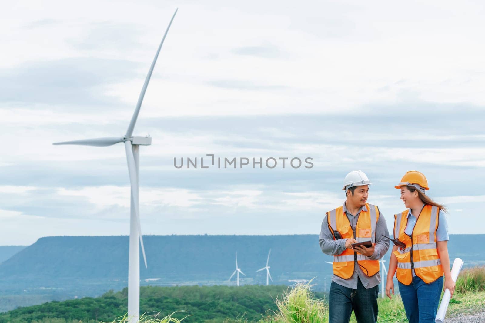 Male and female engineers working on a wind farm atop a hill or mountain in the rural. Progressive ideal for the future production of renewable, sustainable energy.