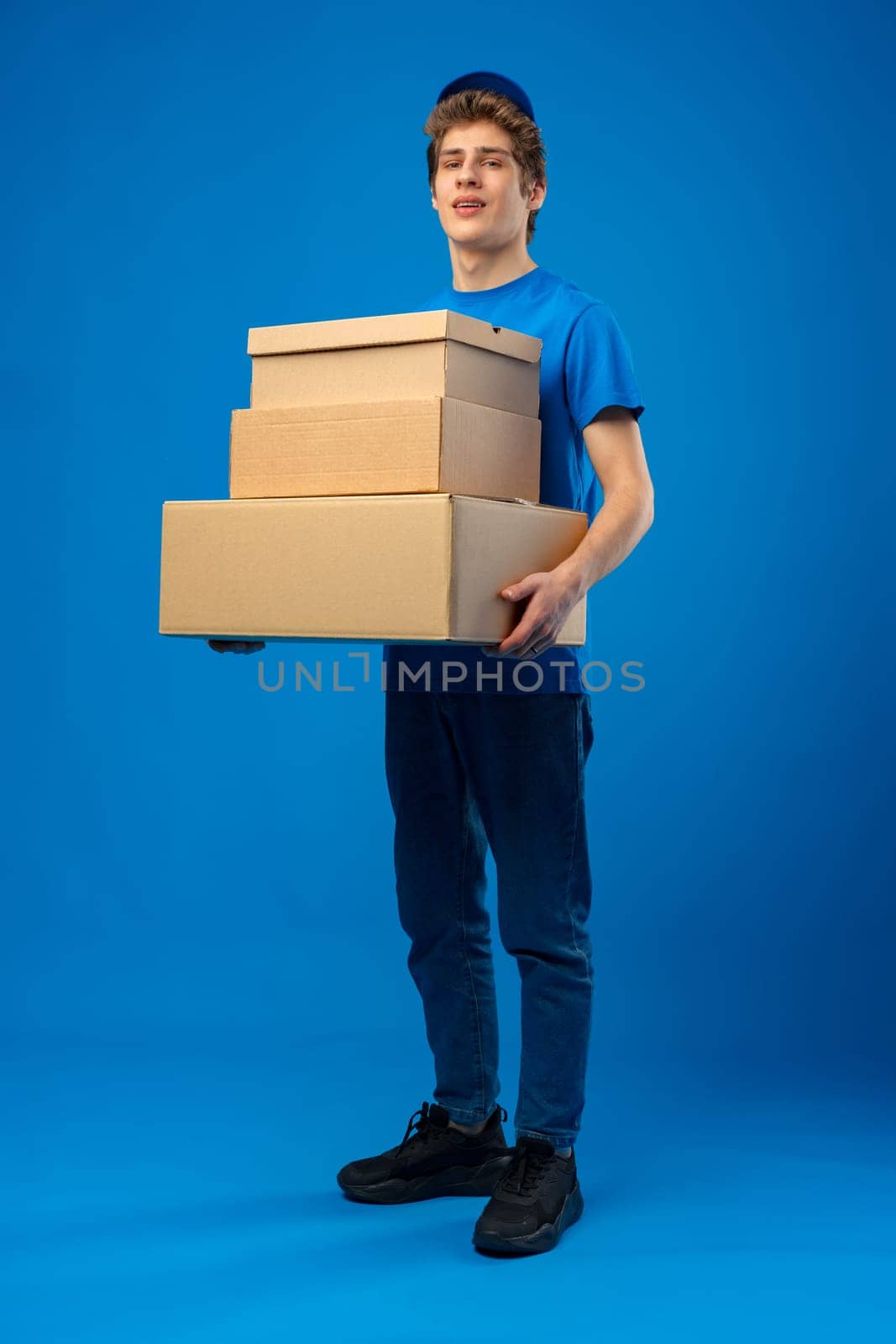 Young male courier in a blue uniform holds parcel in his hands in studio