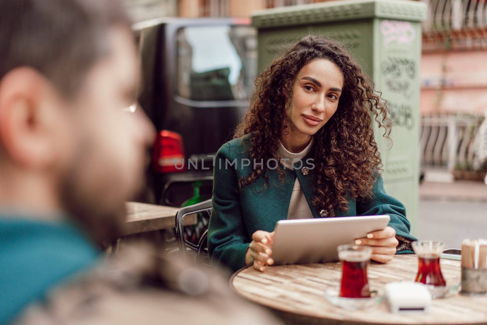 Beautiful curly businesswoman using digital tablet outdoors in cafe by Fabrikasimf