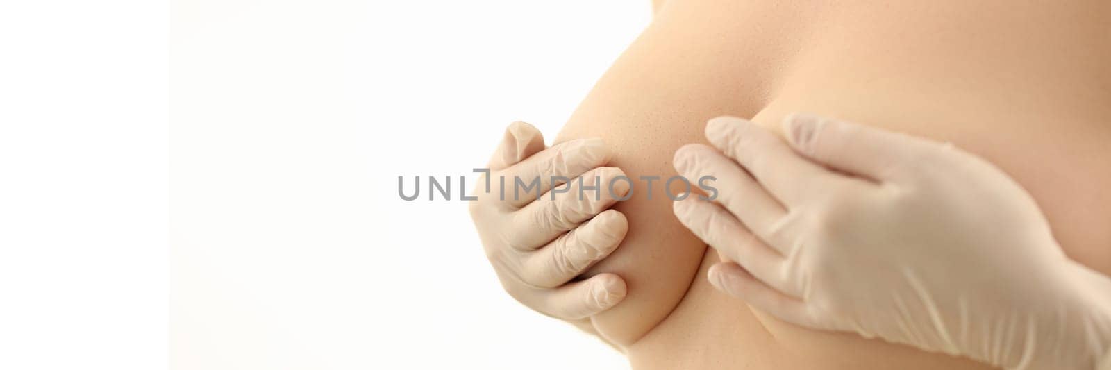 Women hands in rubber gloves cover naked breasts. Breast health and skin care concept and female breast augmentation