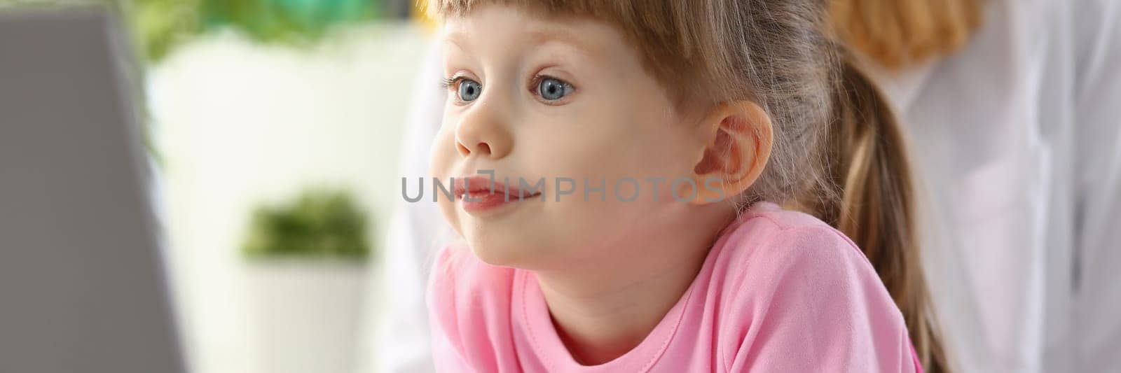 Beautiful little girl child carefully looks at monitor screen. Interesting children educational applications concept